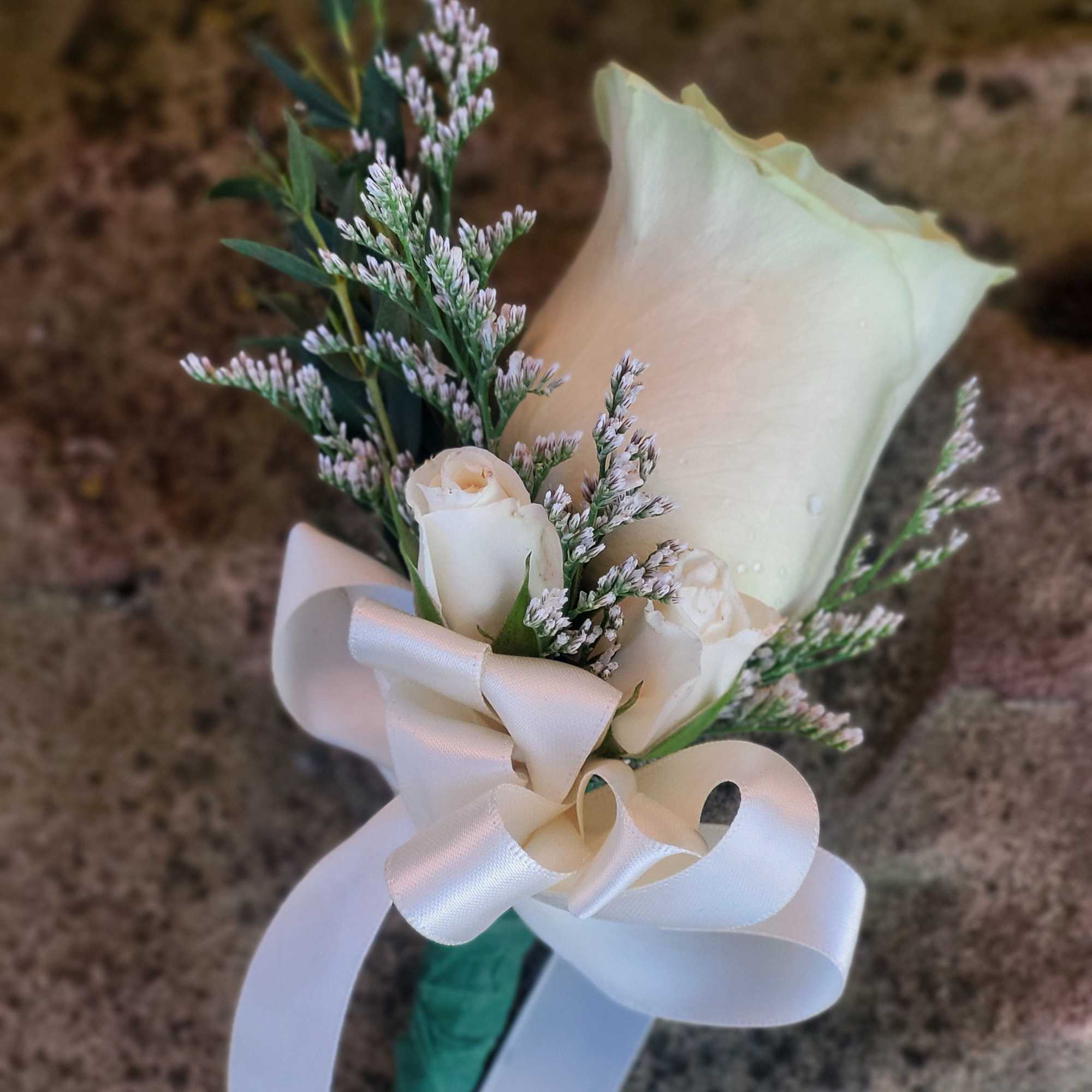 White rose boutonniere with small white filler flowers and a white ribbon bow.