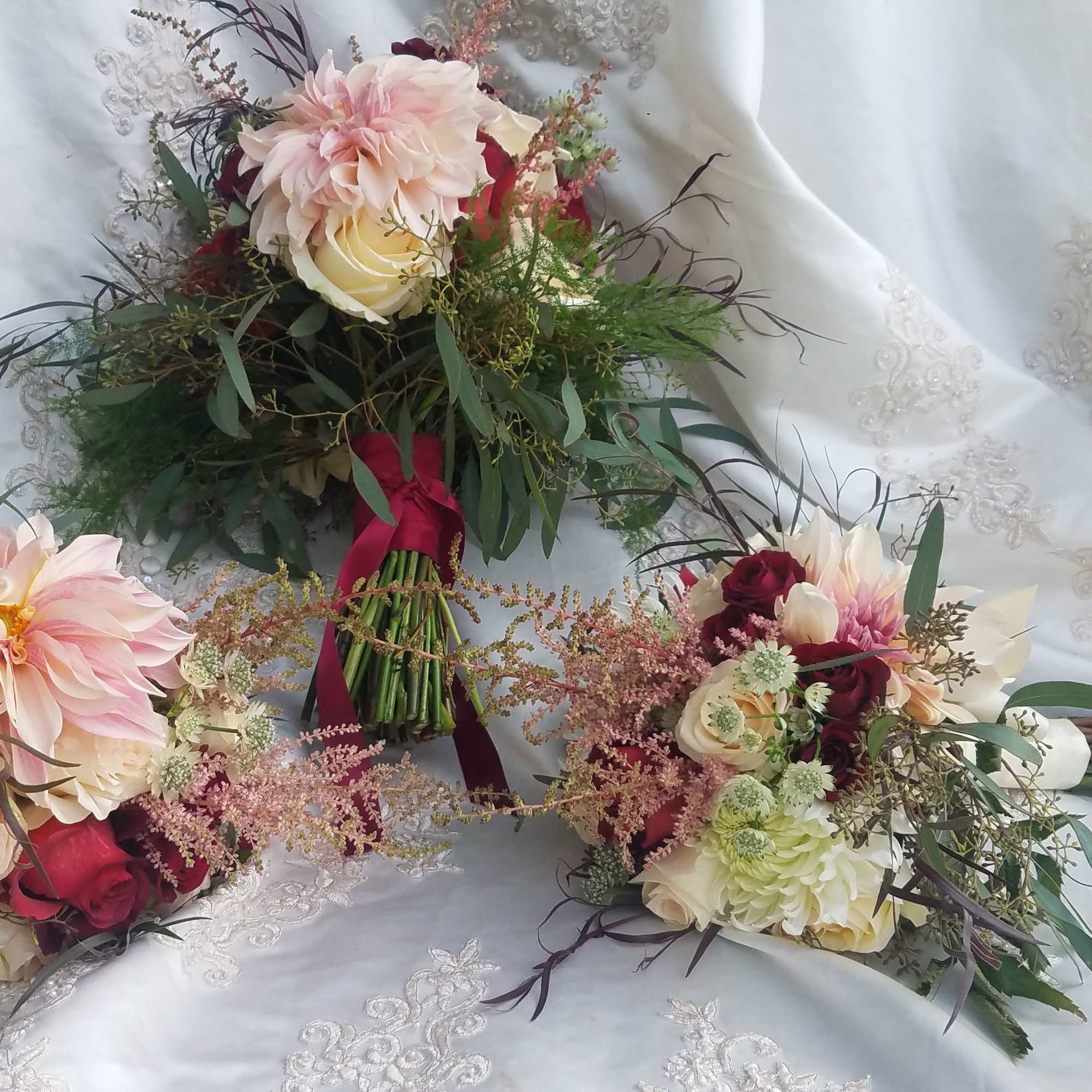 Three bridal bouquets with blush and cream flowers on white fabric