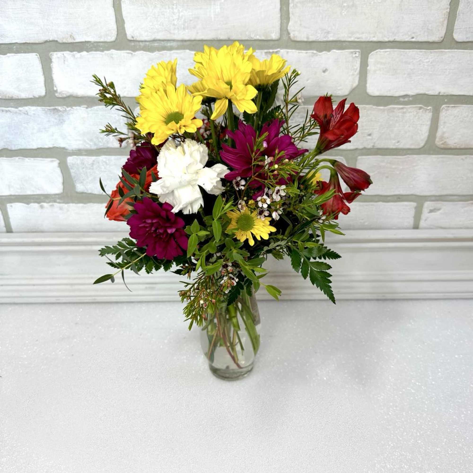 Mixed bouquet of yellow daisies, red alstroemeria, and white carnation in a clear glass vase