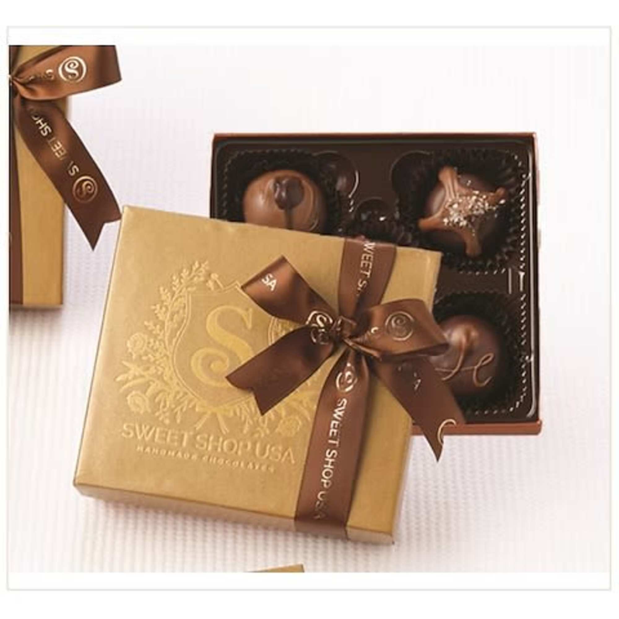 Gold gift box of assorted chocolates with brown ribbon and open tray of truffles.