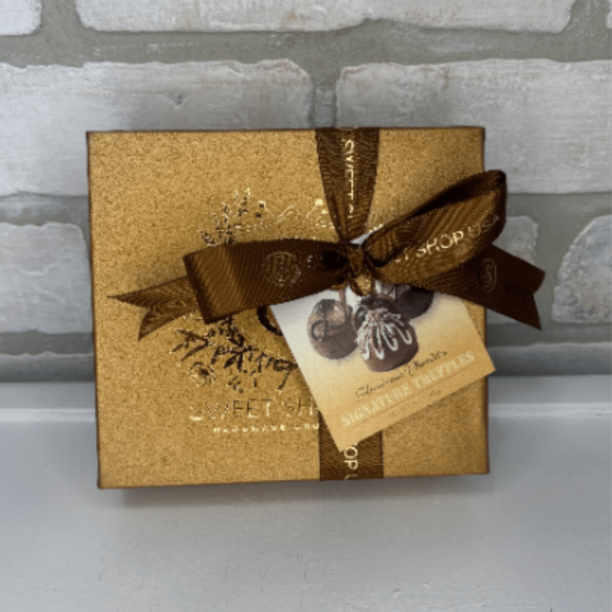 Gold chocolate gift box with brown ribbon and truffle tag
