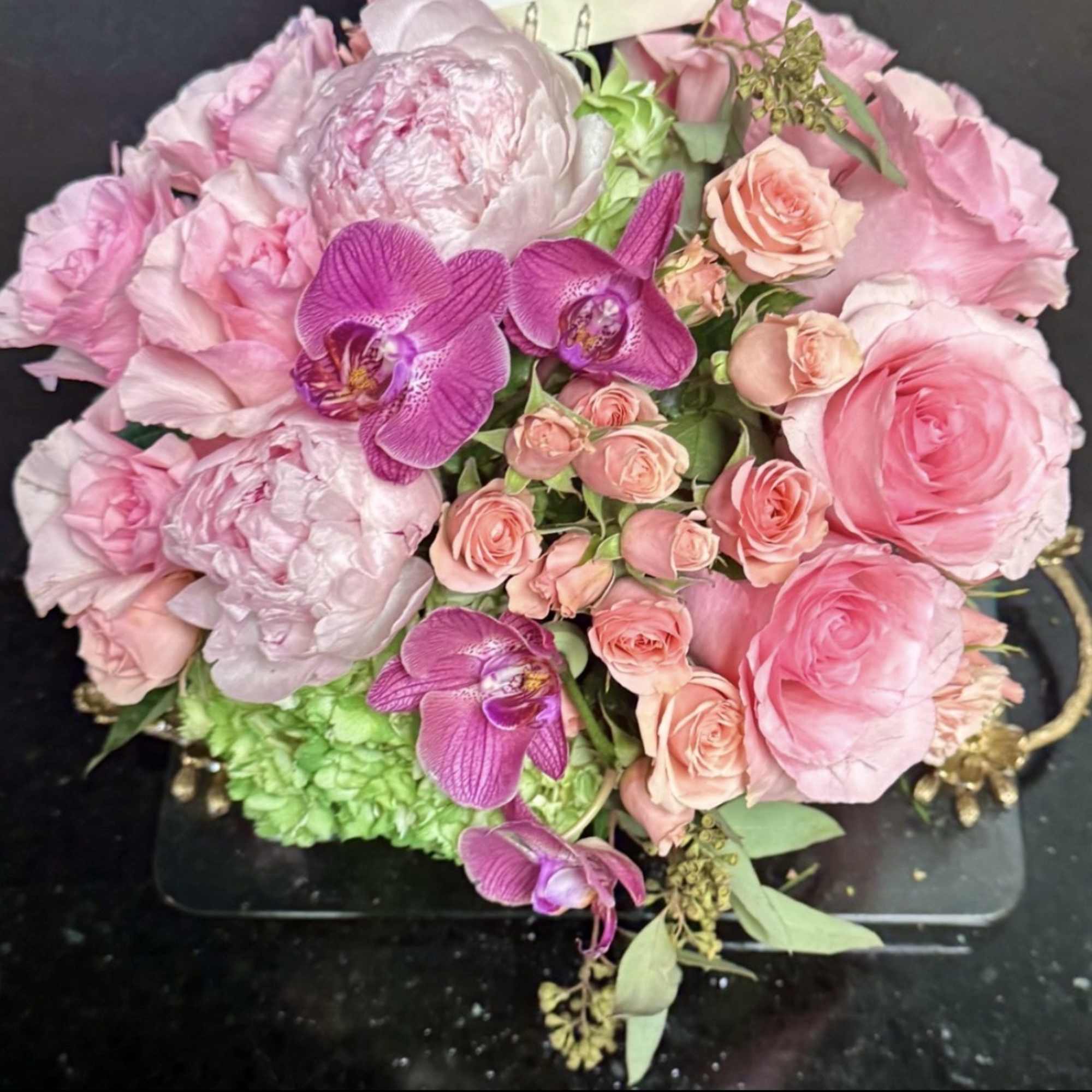 Pink floral arrangement with roses, orchids, and peonies in a low container