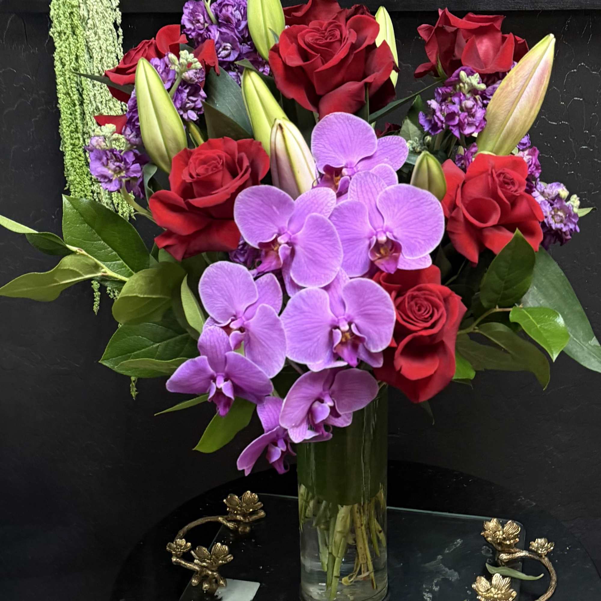 Bouquet of red roses, purple orchids, and lilies in a glass vase
