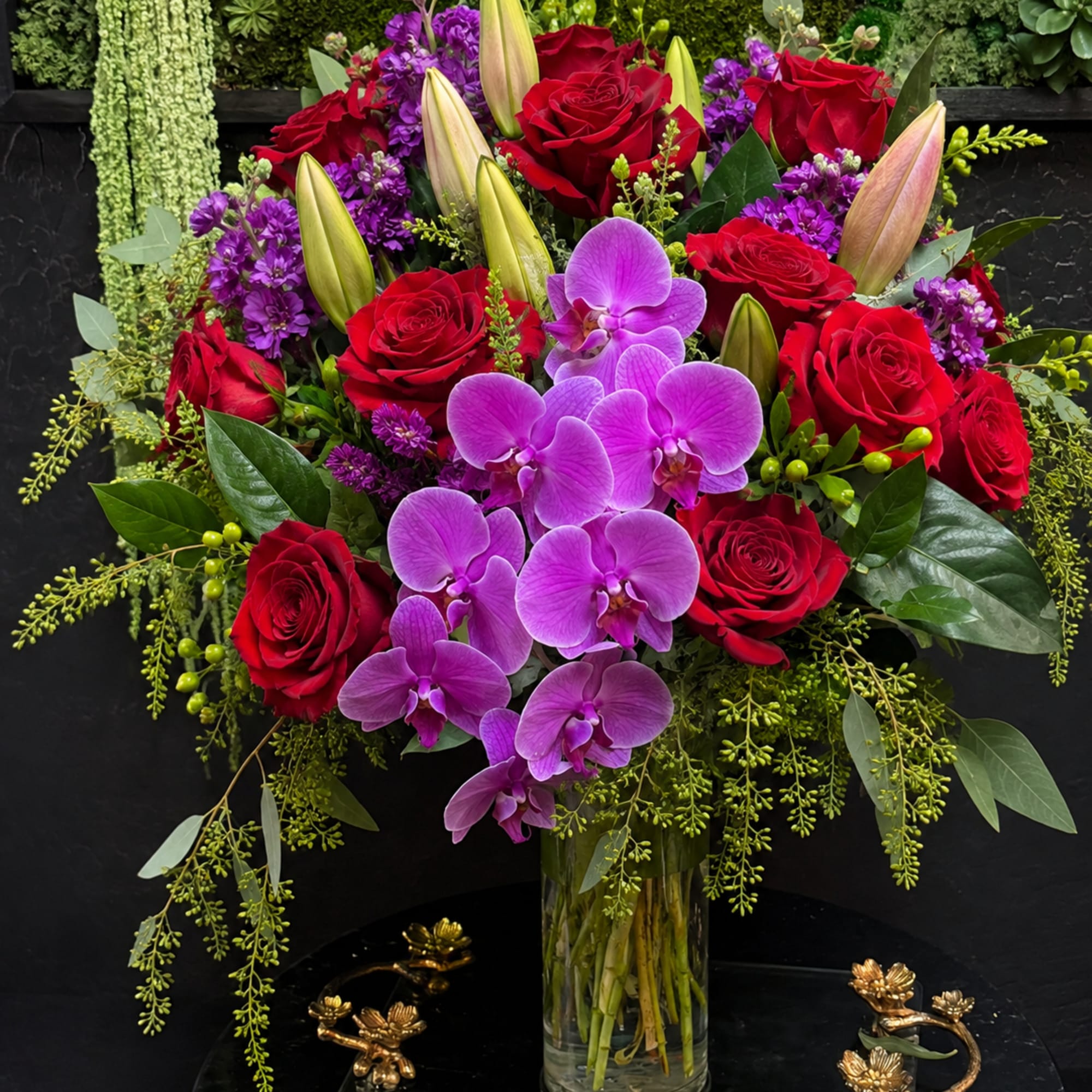 Bouquet of red roses, purple orchids, and lilies in a glass vase