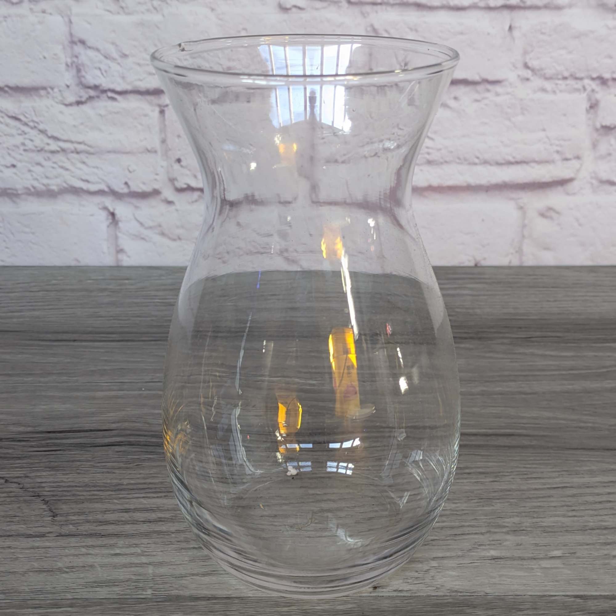 Clear glass vase with a narrow waist on a wood surface
