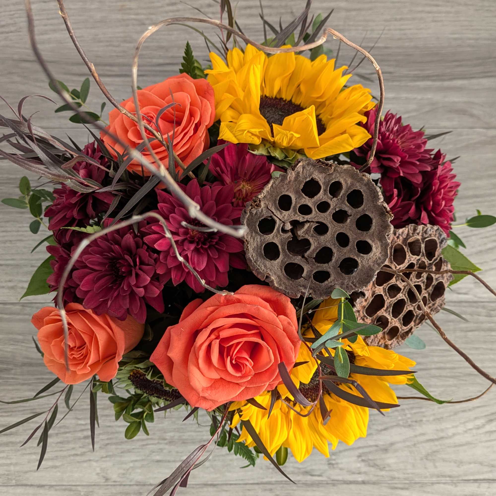 Bouquet of orange roses, yellow sunflowers, and burgundy mums with dried lotus pods