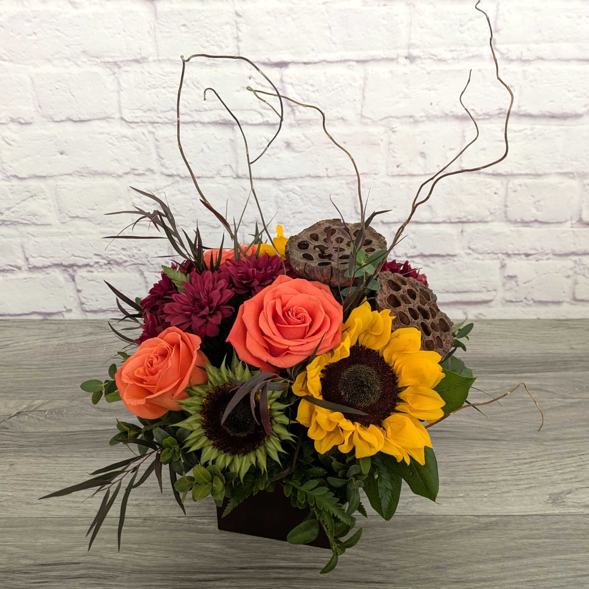 Arrangement of orange roses, sunflowers, and burgundy mums in a low container