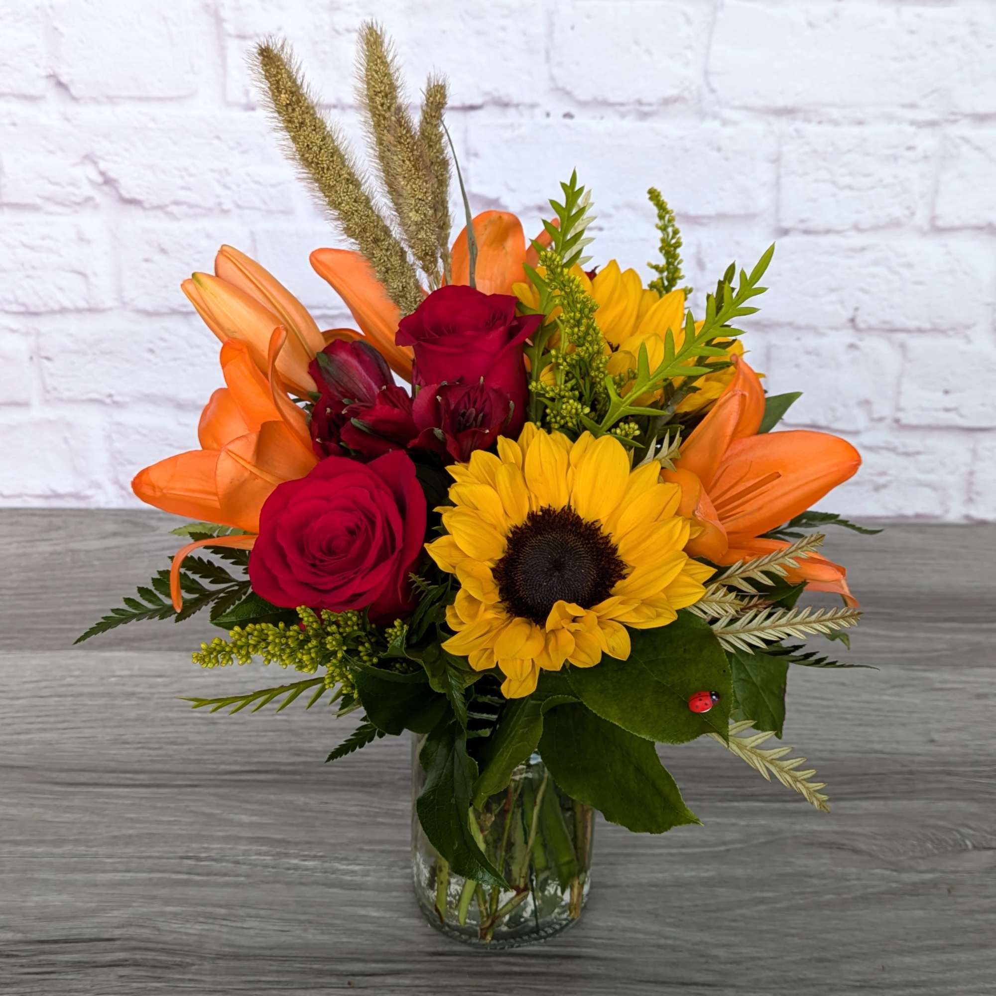 Bouquet of sunflowers, red roses, orange lilies, and alstroemeria in a glass vase