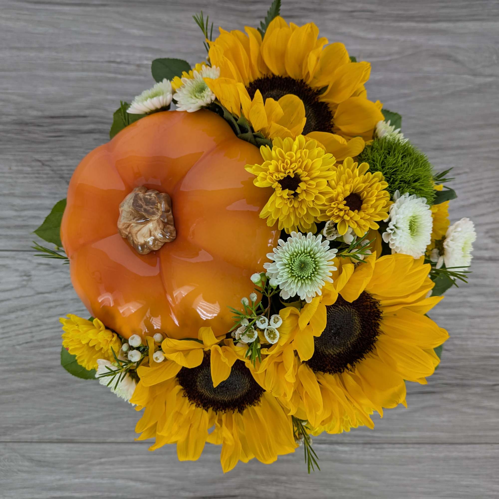 Sunflowers and yellow mums arranged around an orange pumpkin centerpiece