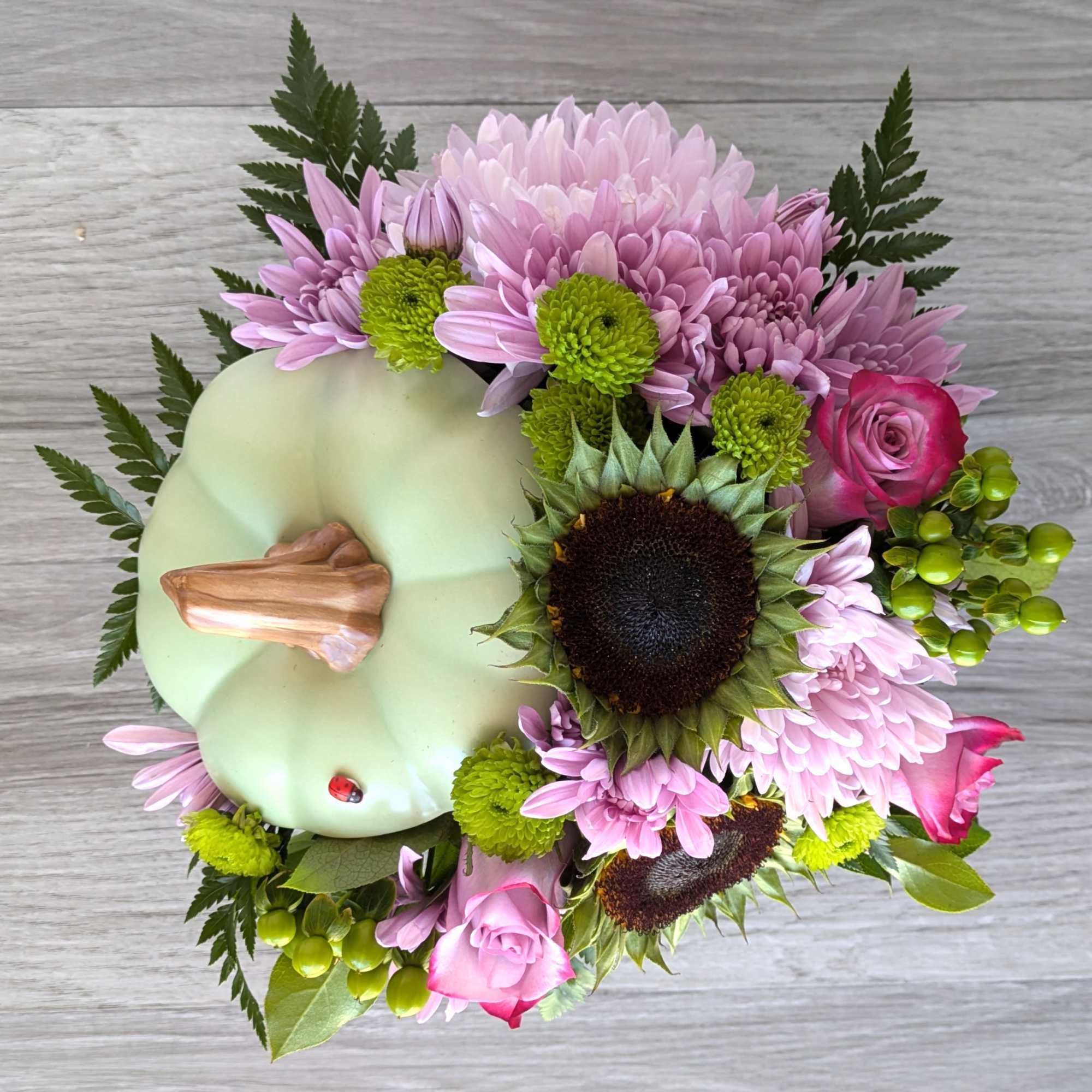 Pumpkin-shaped arrangement with pink chrysanthemums, roses, and a sunflower