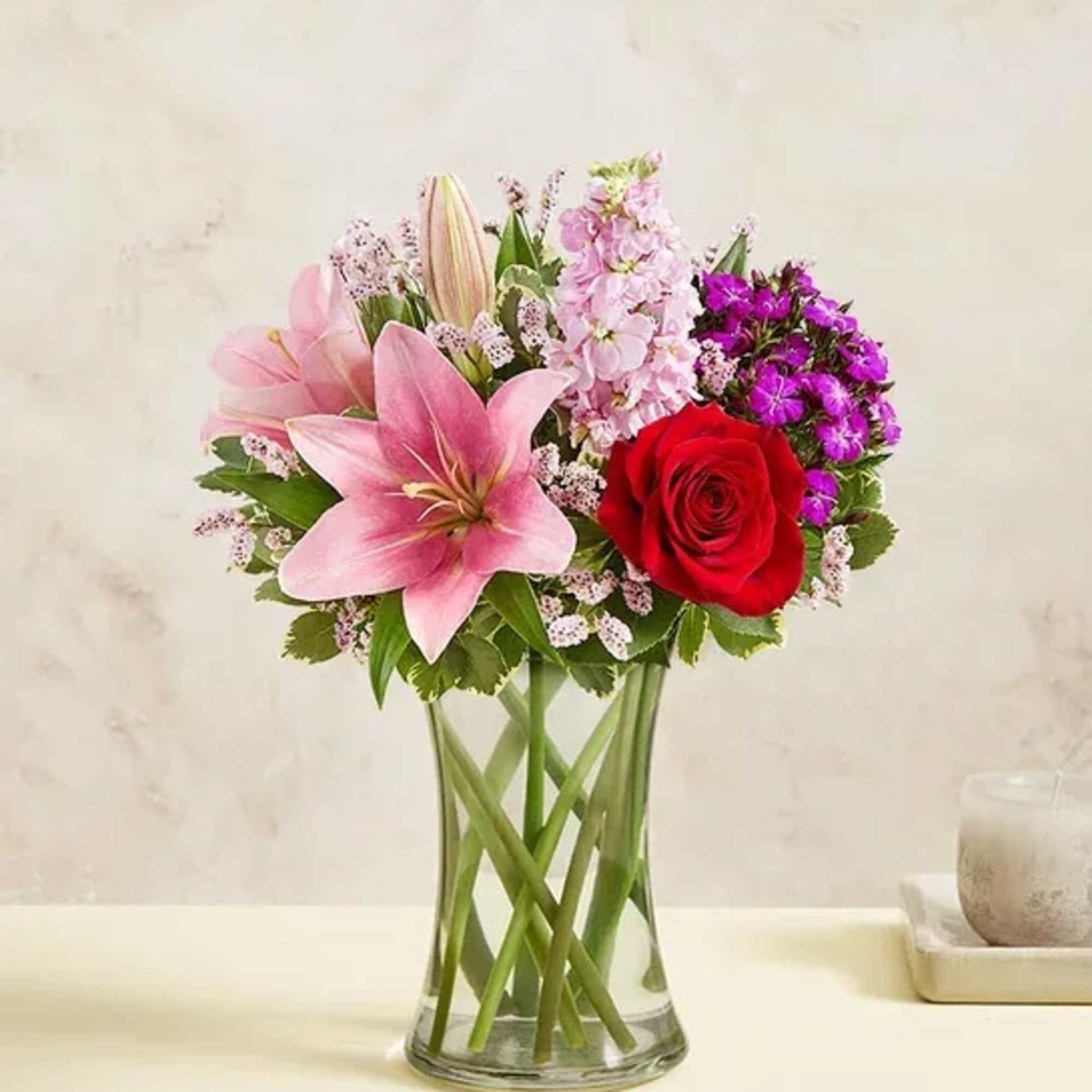 Pink lilies and a red rose in a clear glass vase