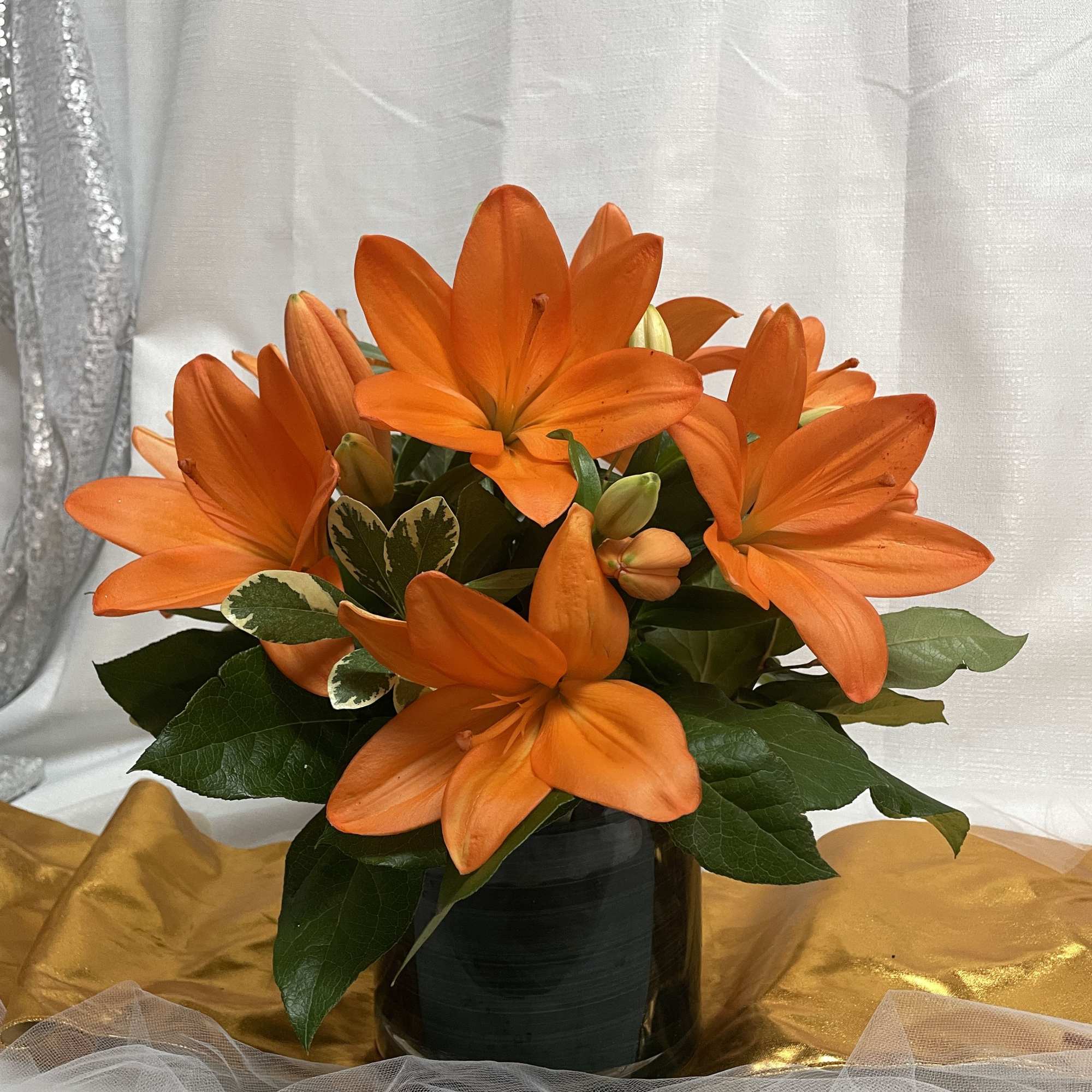 Orange lilies arranged in a black vase with dark green foliage