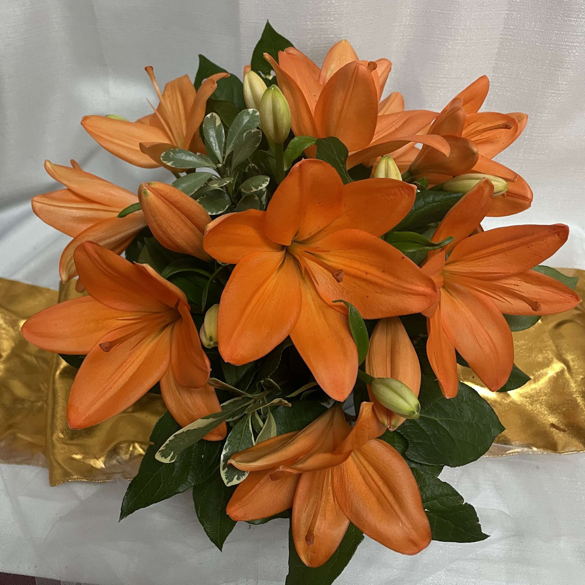 Bouquet of orange lilies with green foliage and gold wrapping