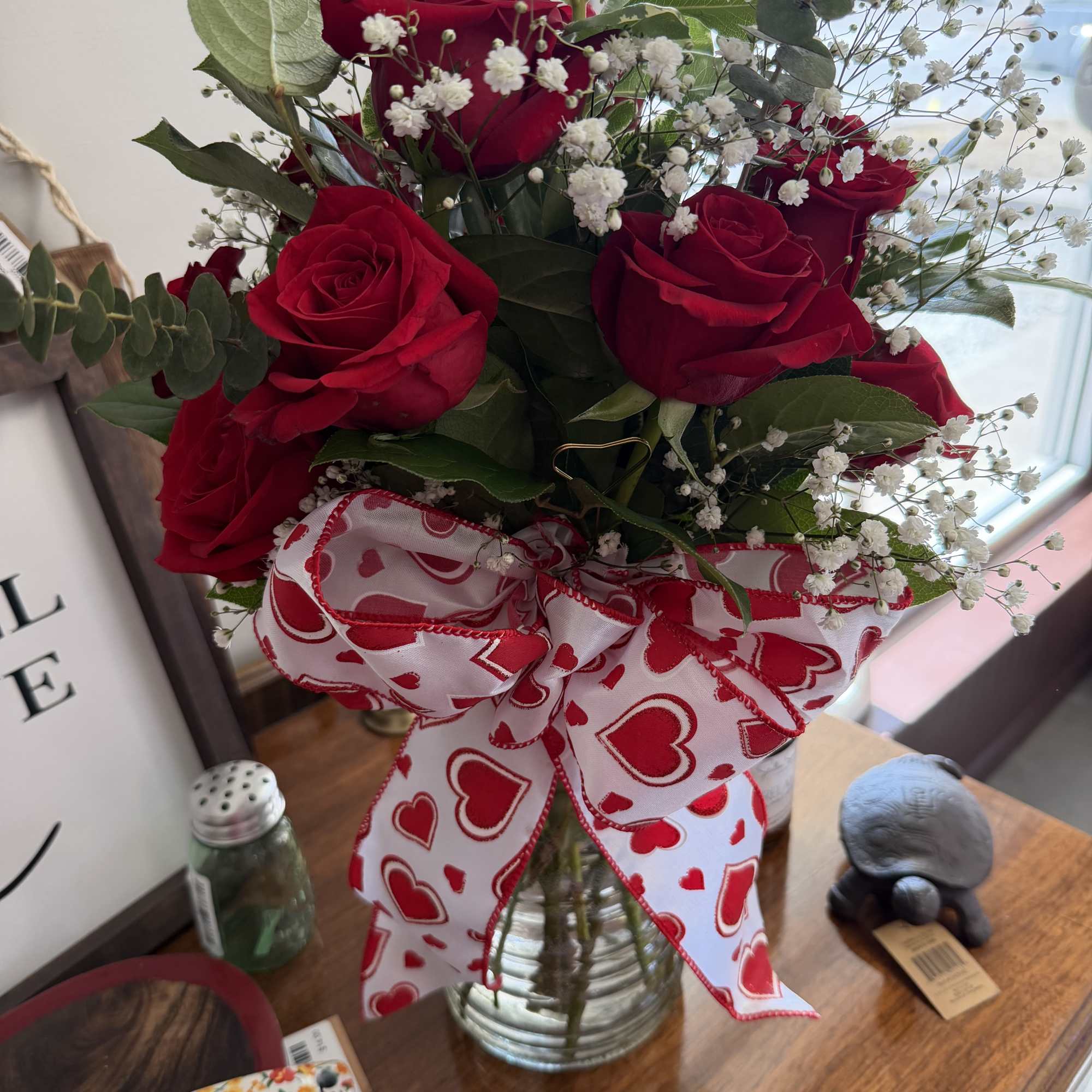 Bouquet of red roses and baby's breath in a glass vase with a heart ribbon