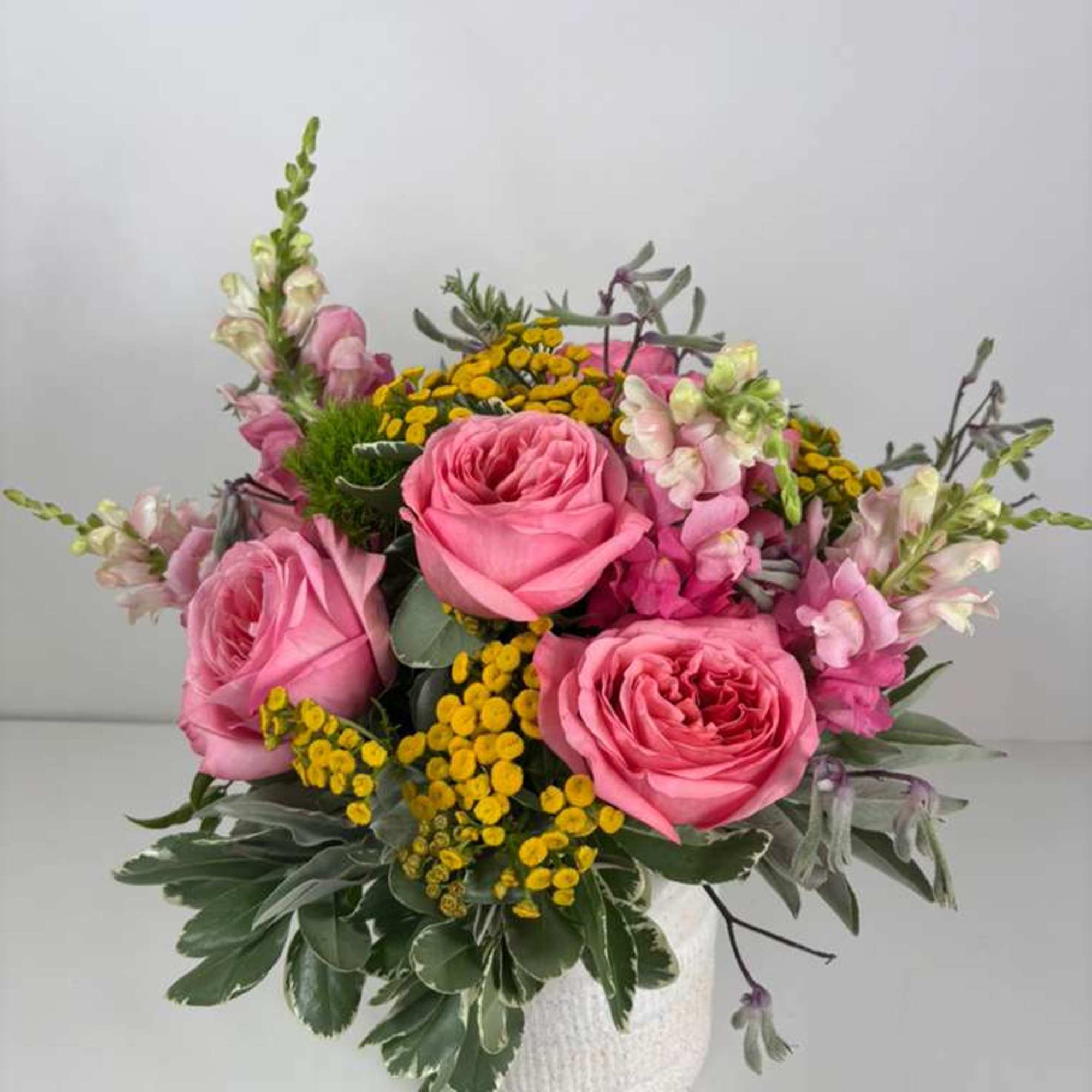 Pink roses and yellow button flowers in a white vase