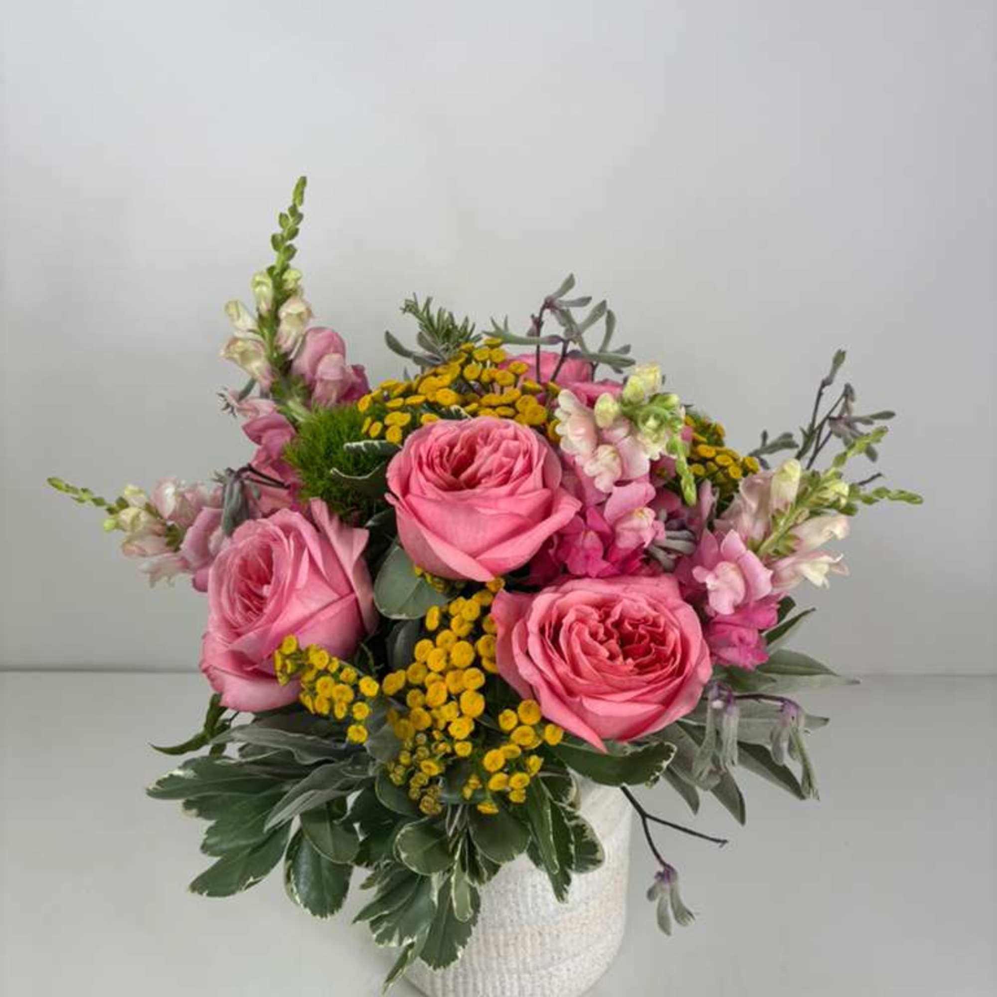 Pink roses and yellow filler flowers in a white vase