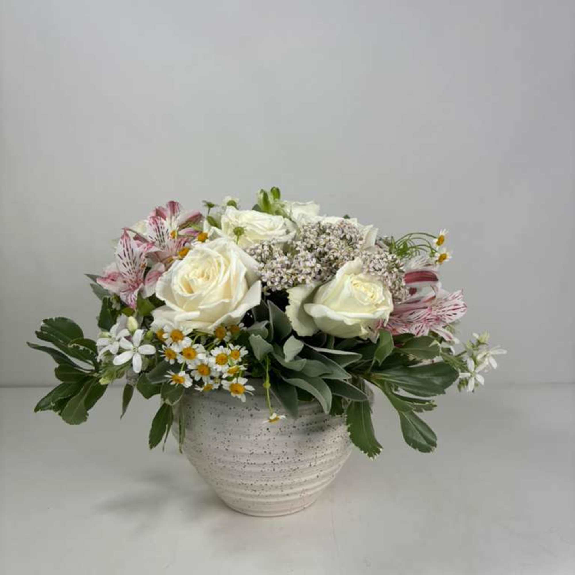 White roses and pink alstroemeria in a white ceramic vase