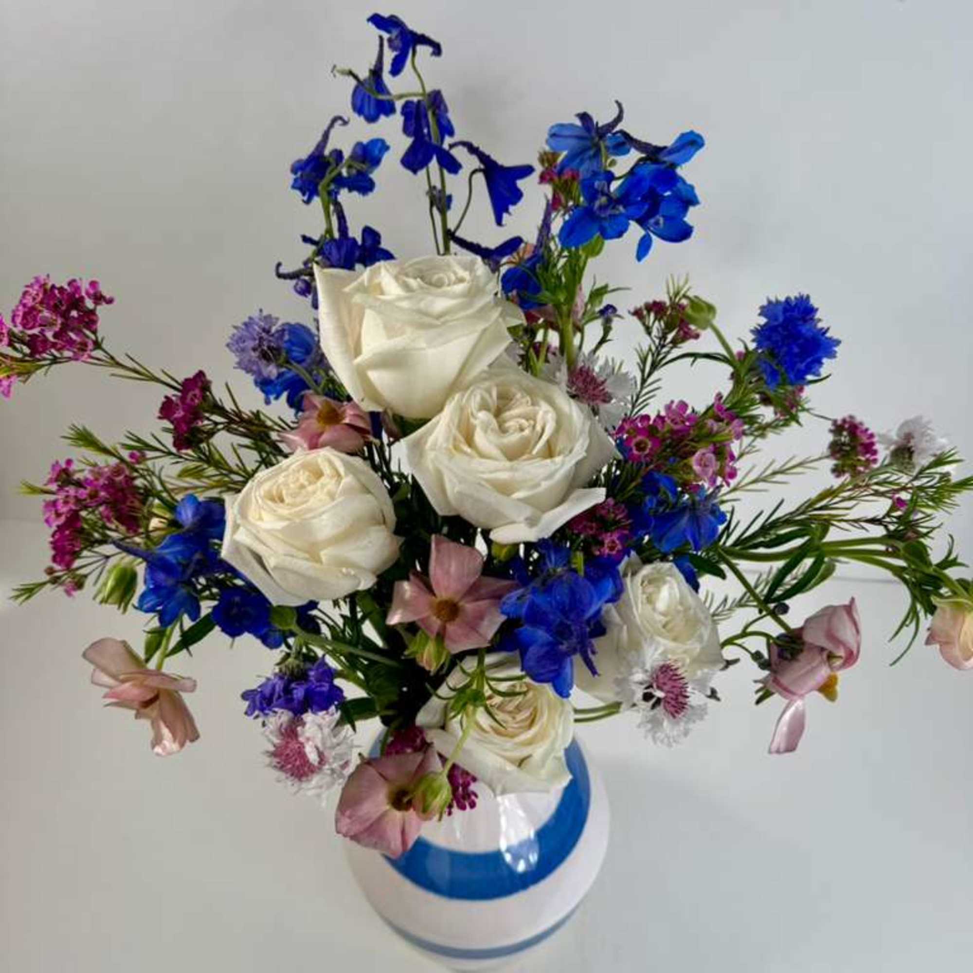 Bouquet of white roses and blue flowers in a white vase