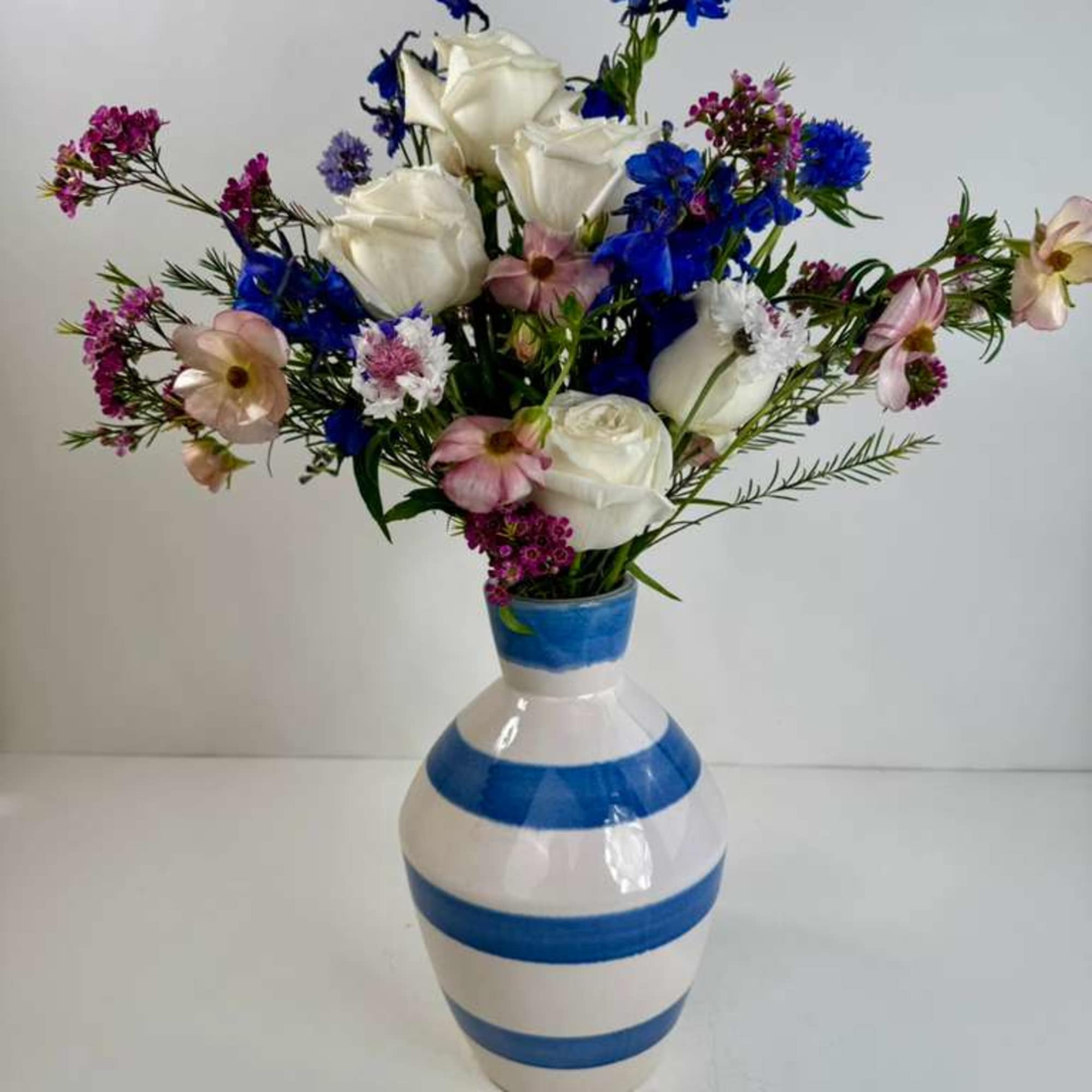 Bouquet of white roses, blue flowers, and pink accents in a striped vase