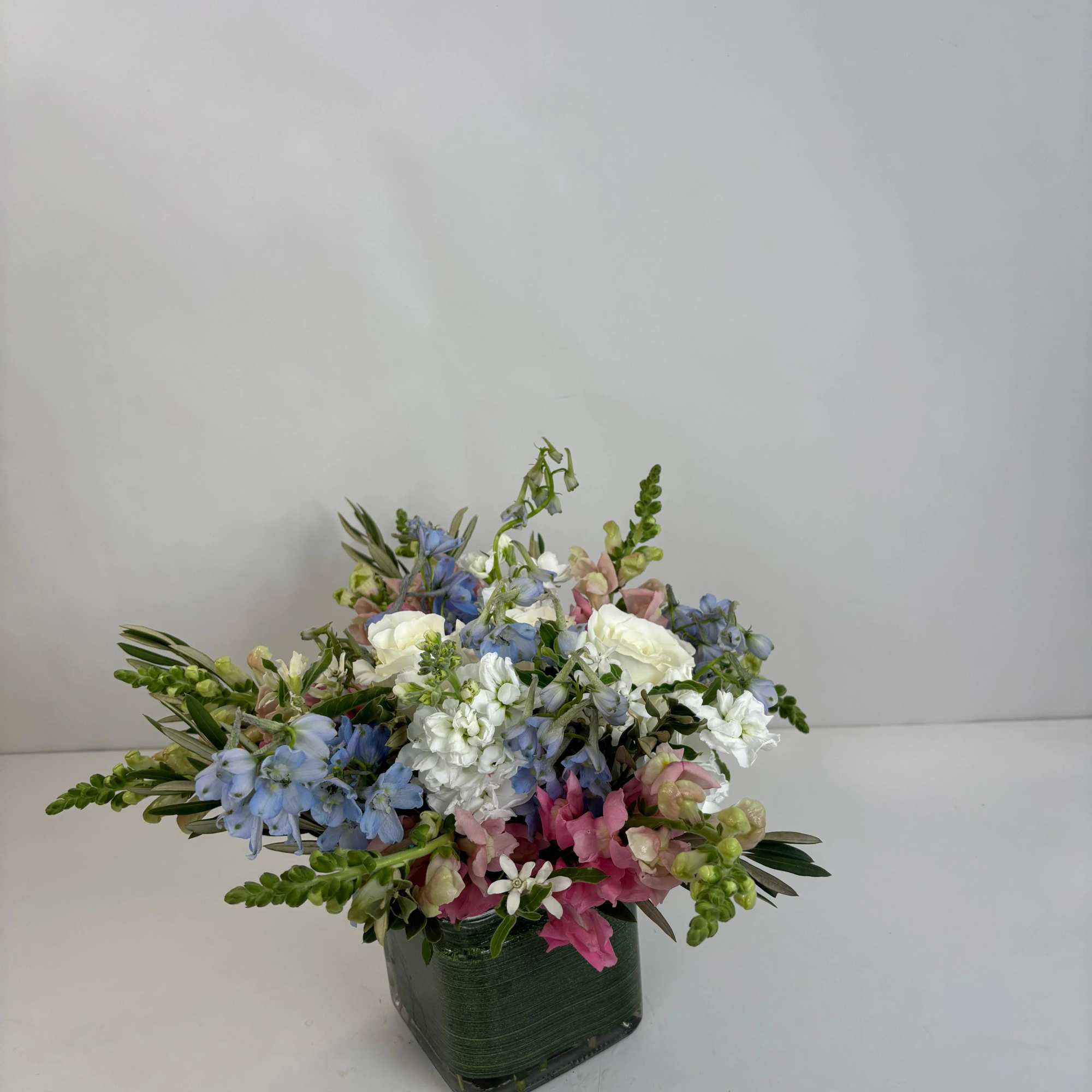 Mixed bouquet of blue, white, and pink flowers in a square green vase