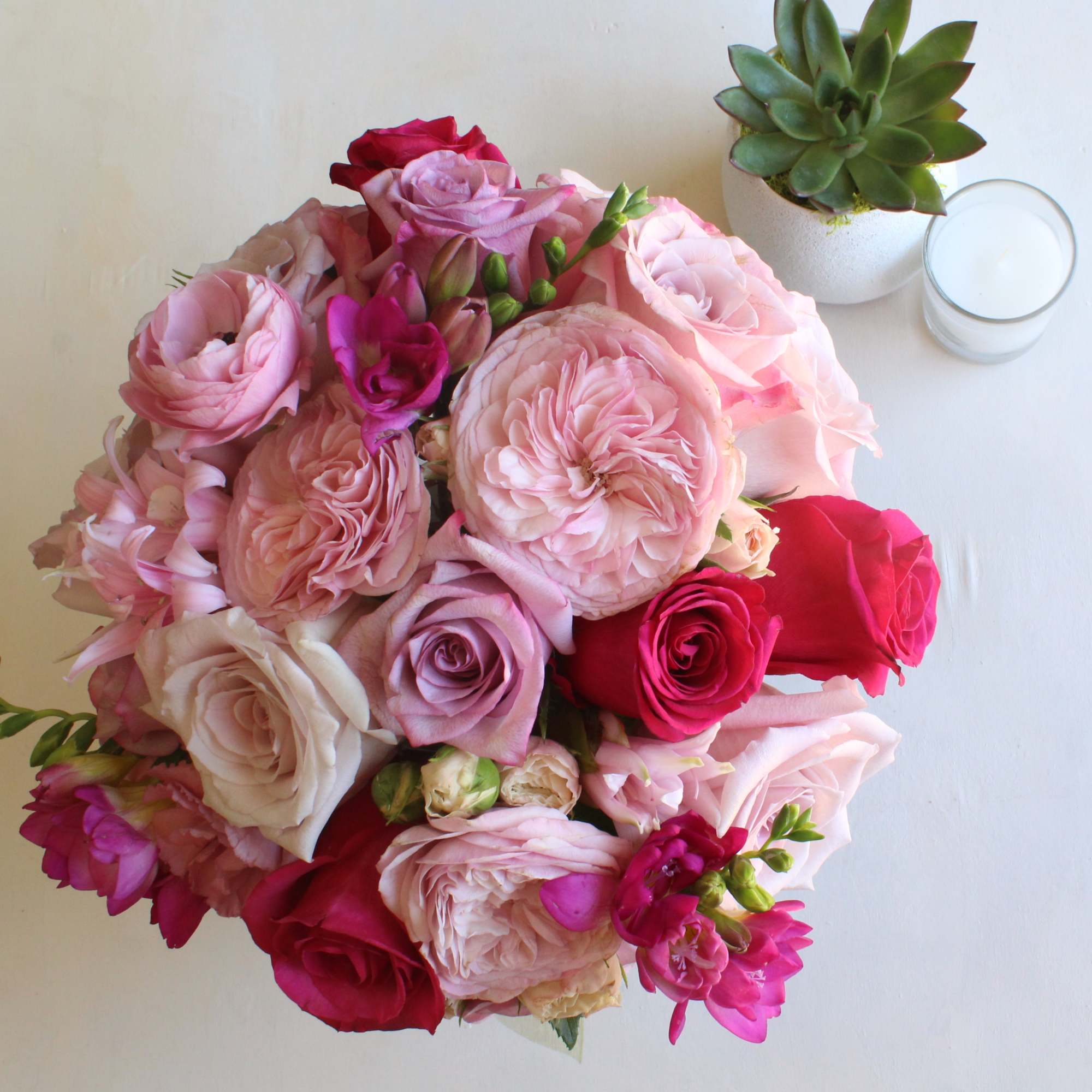 Bouquet of pink and red roses with a small succulent and candle nearby