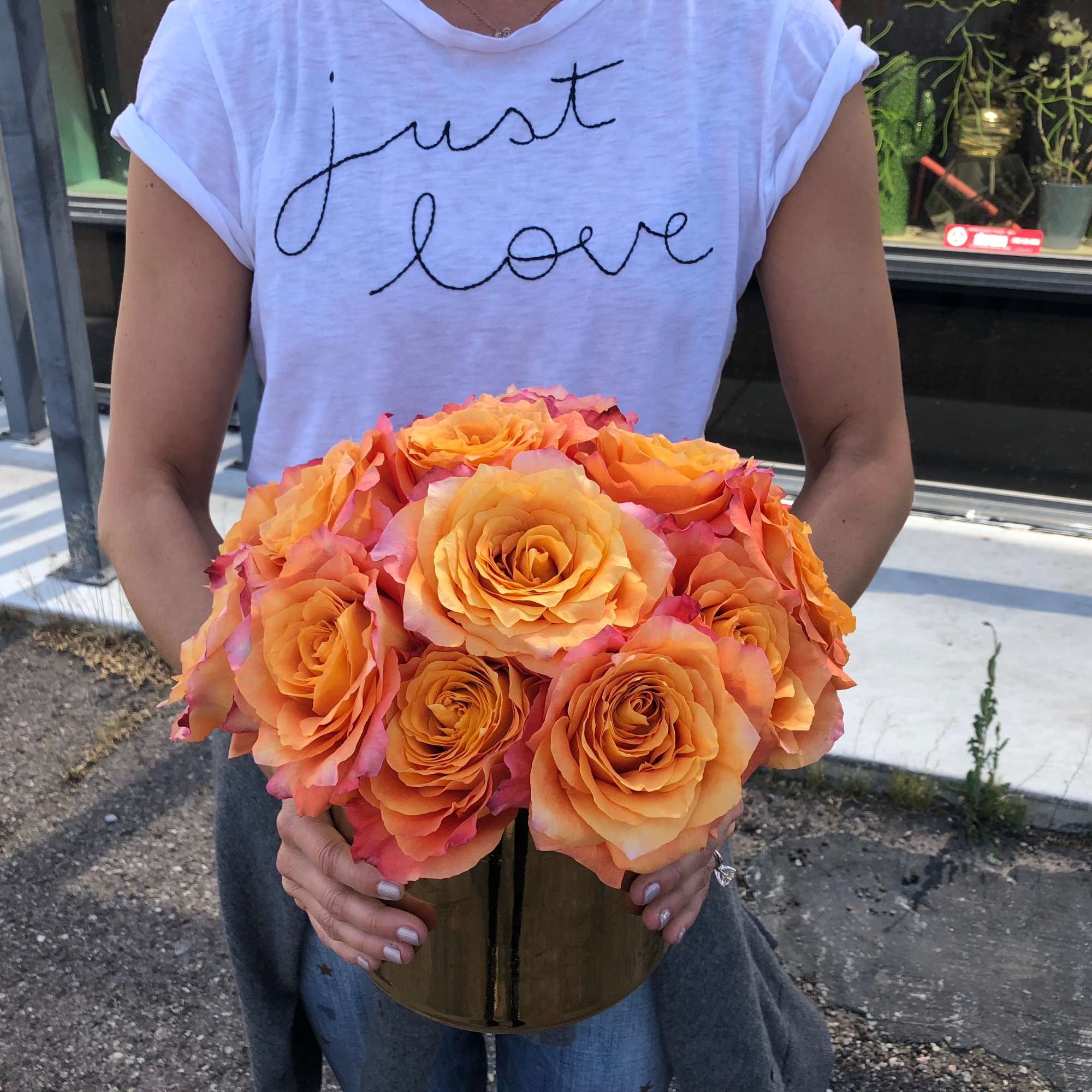 Person holding a round bouquet of orange and pink roses in a gold vase