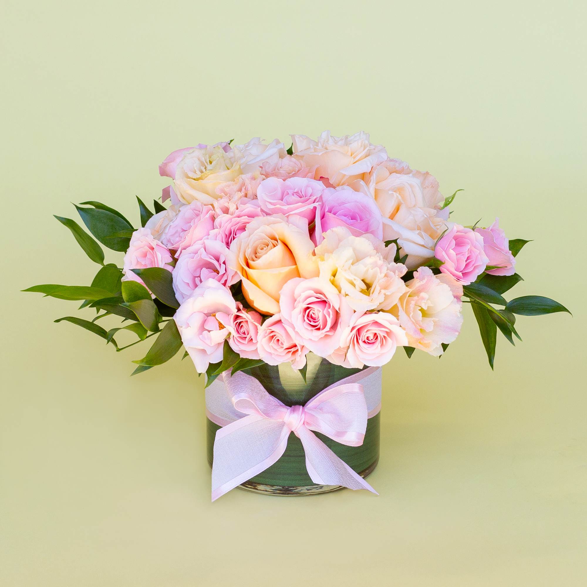 Pink and peach roses arranged in a round vase with a pink ribbon