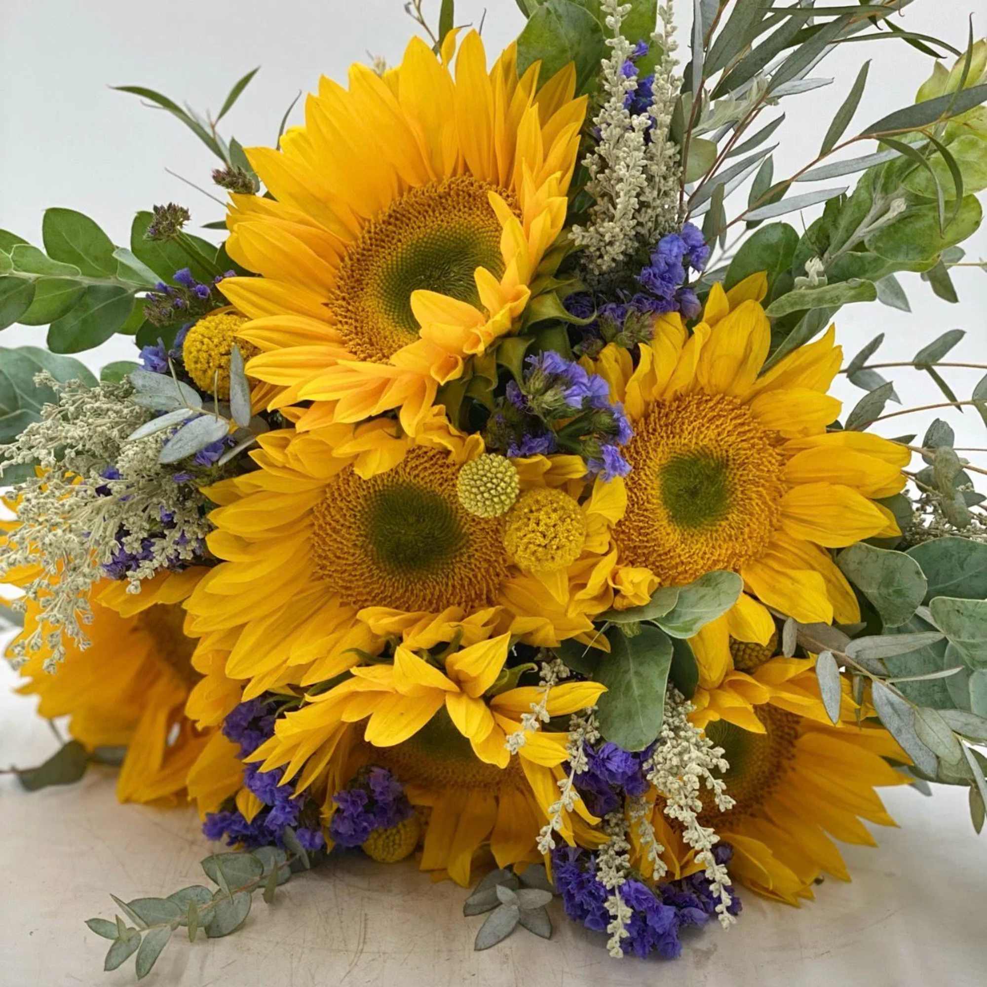 Bouquet of bright yellow sunflowers with purple accents and greenery