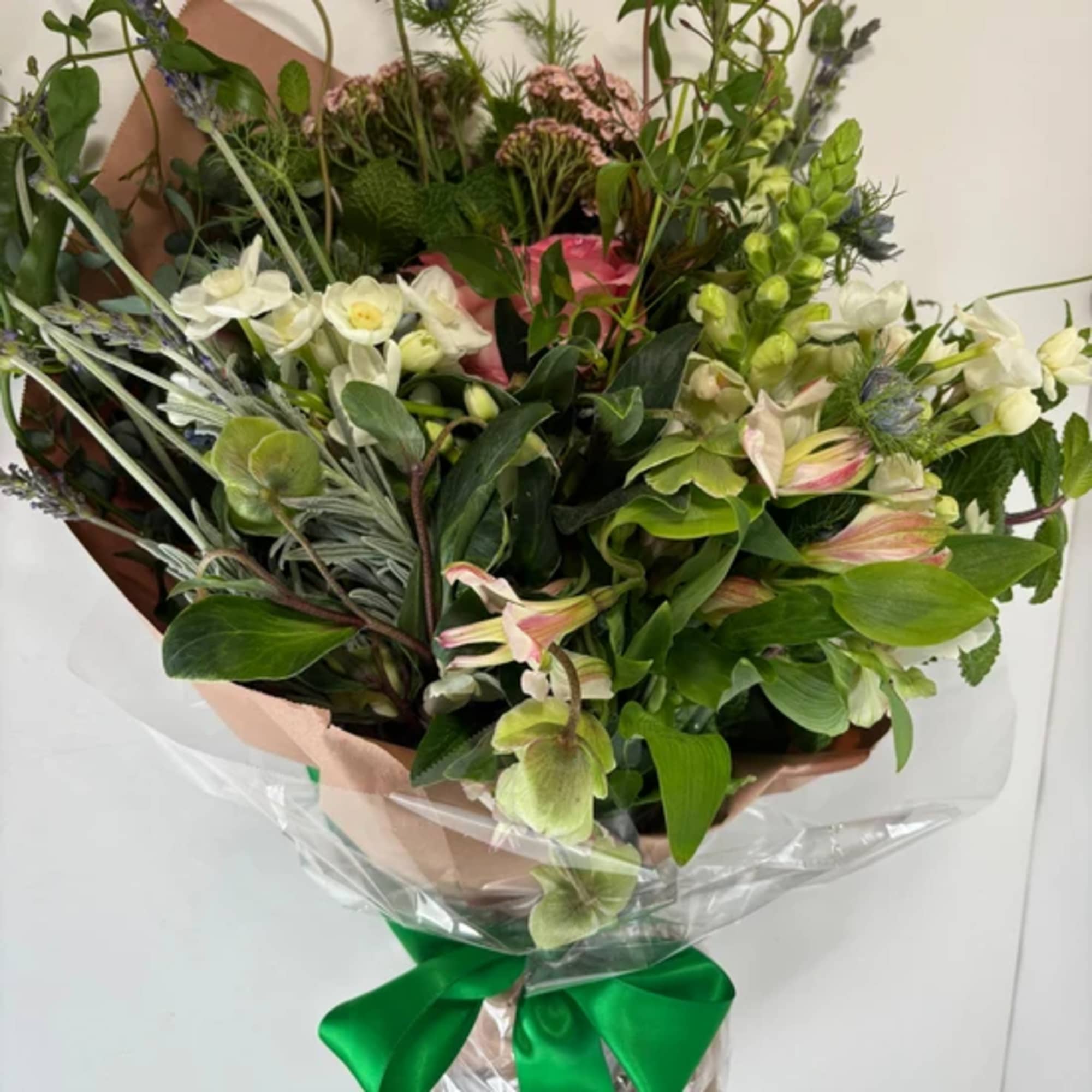 Bouquet of mixed flowers with white blooms and green accents, wrapped in paper with a green ribbon