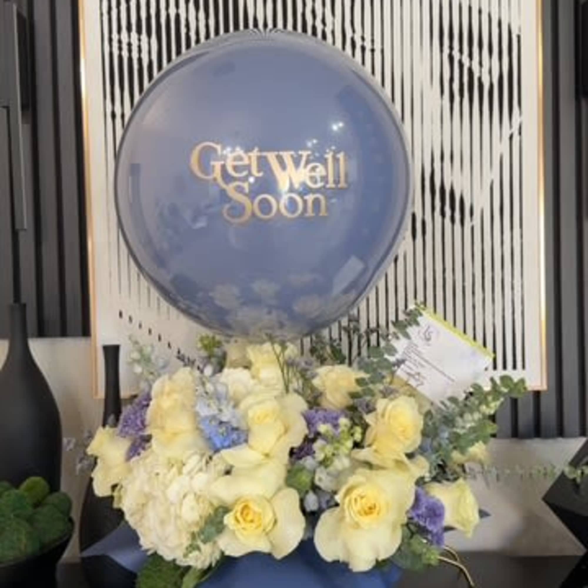 Blue get well soon balloon above a pastel flower arrangement
