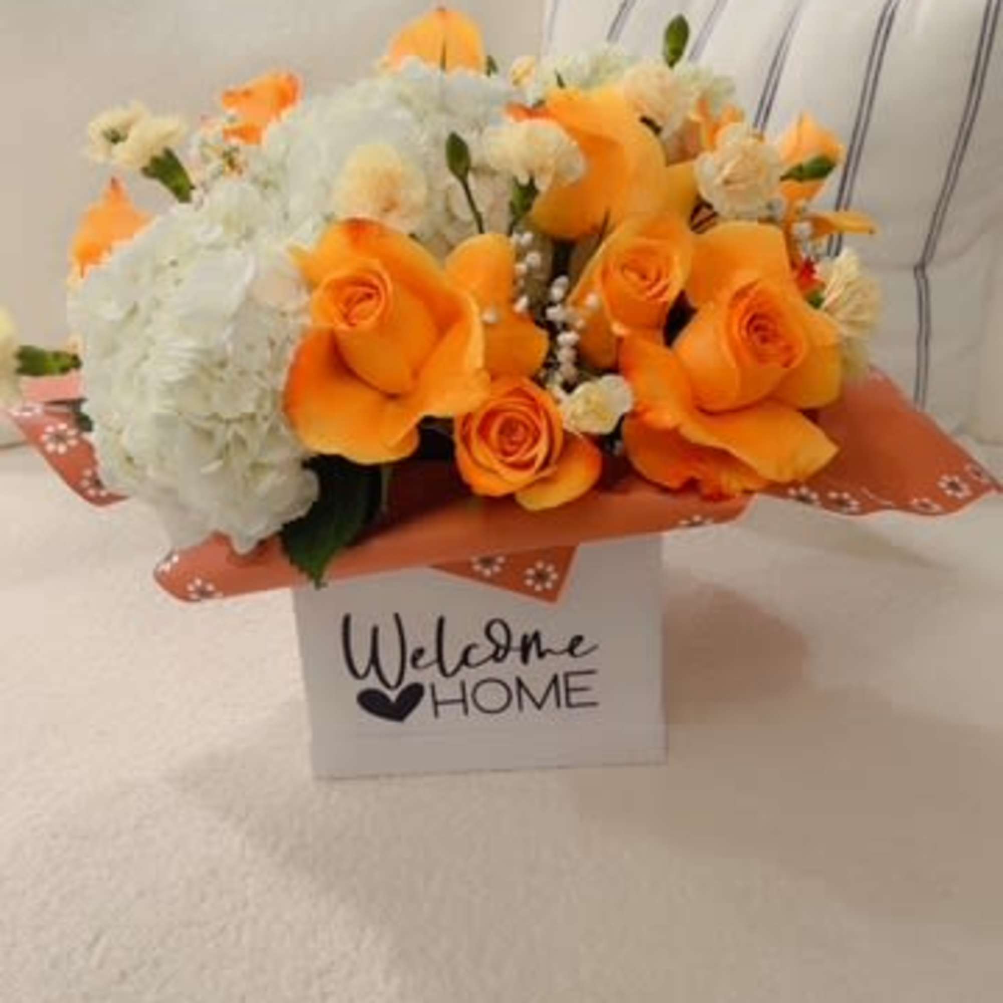 Orange roses and white hydrangeas in a gift box with a "Welcome Home" sign