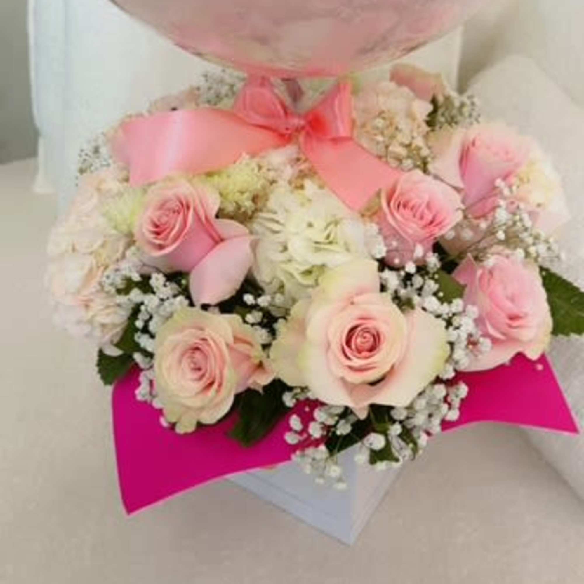 Pink balloon above a bouquet of pale pink roses in a gift box