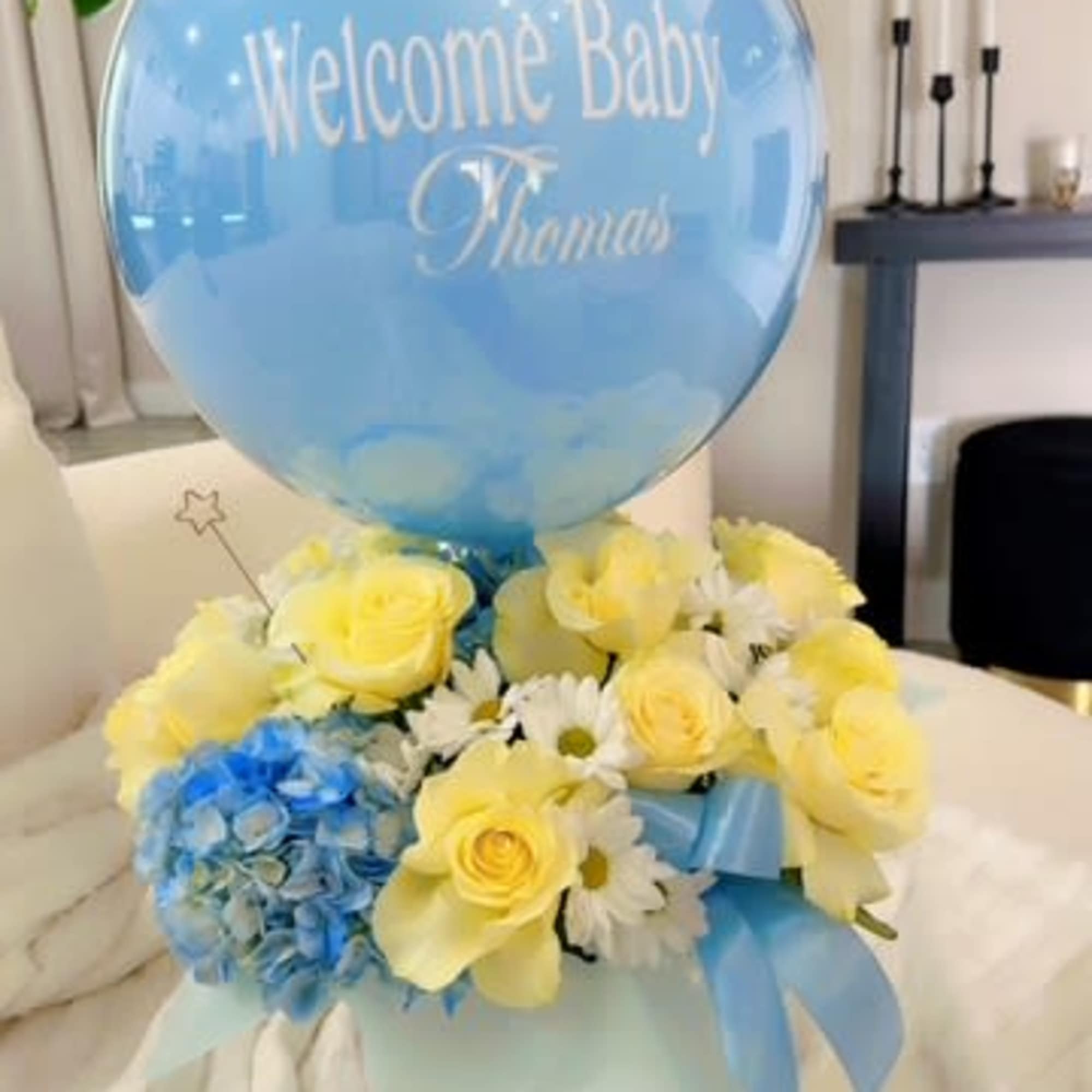 Blue baby balloon above yellow and white flowers in a gift box