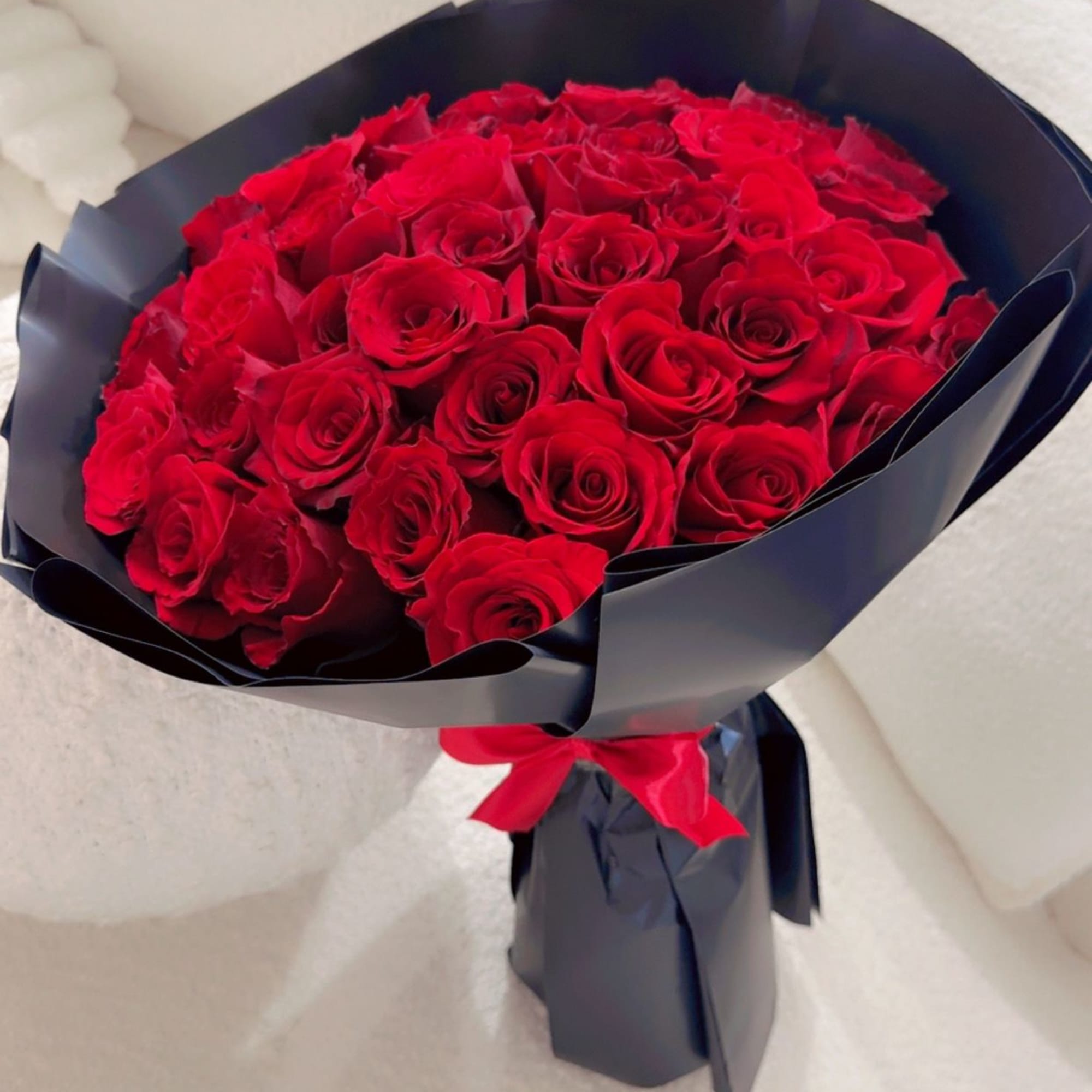 Bouquet of red roses wrapped in dark paper with a red ribbon