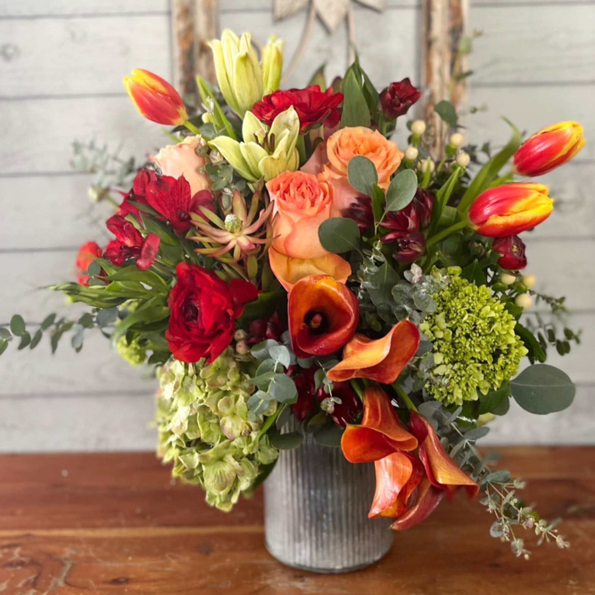 Mixed bouquet in a gray vase with red, orange, and green flowers