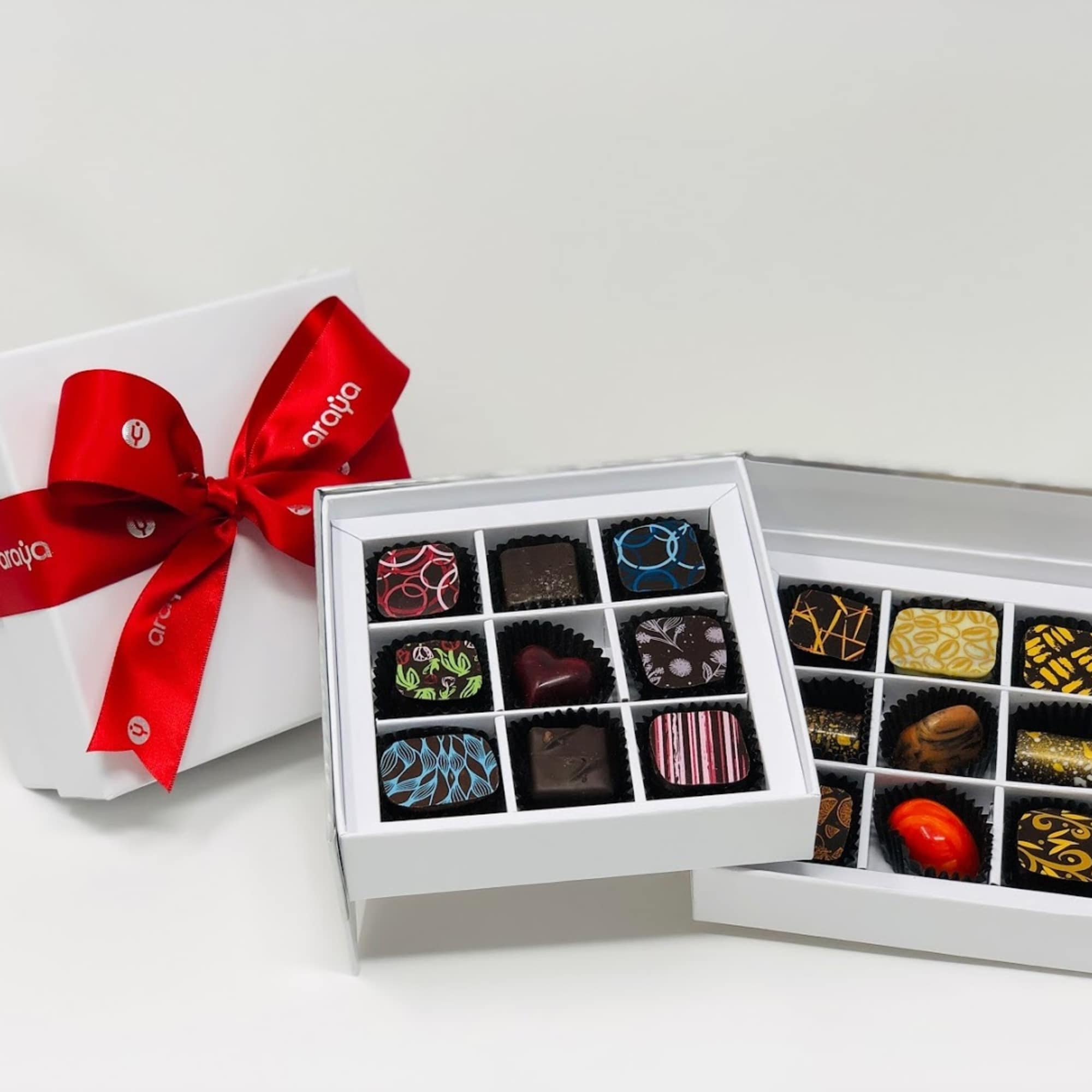 Two boxes of assorted chocolates with a red ribbon on a white gift box