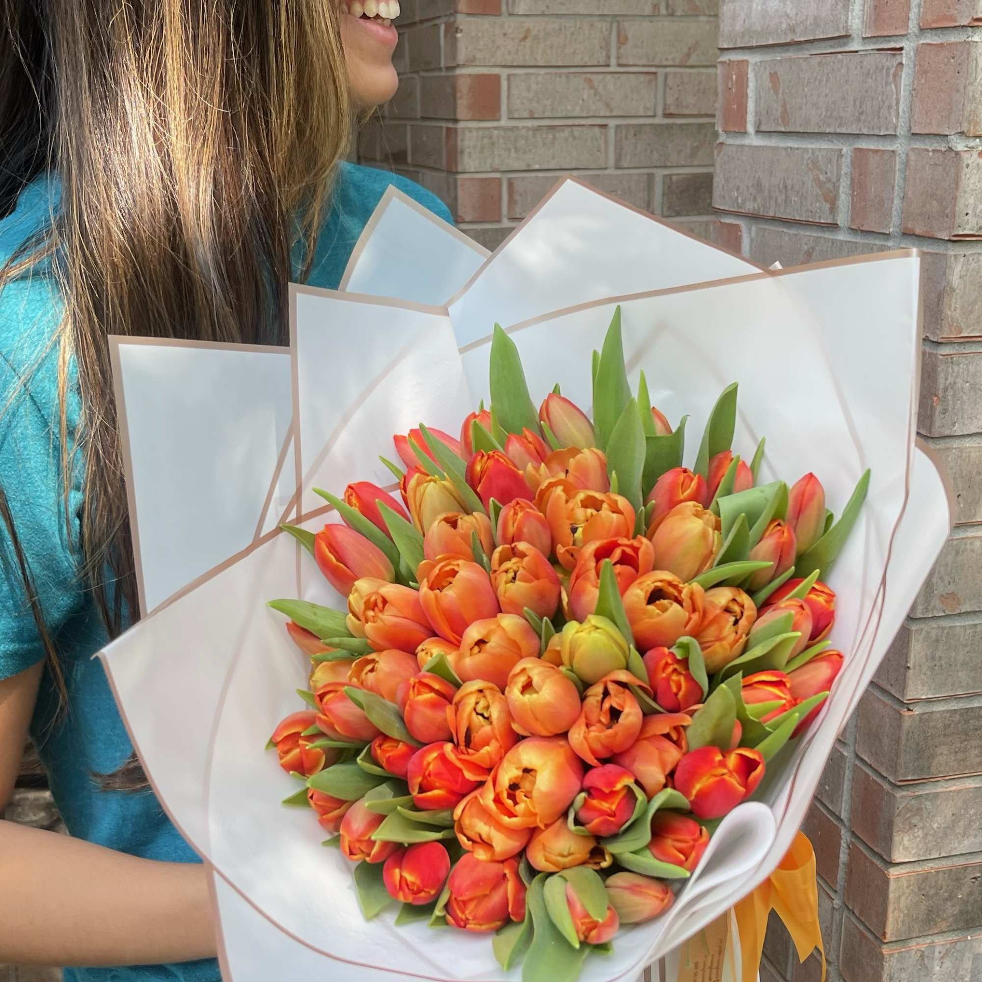Woman holding a bouquet of orange tulips wrapped in white paper