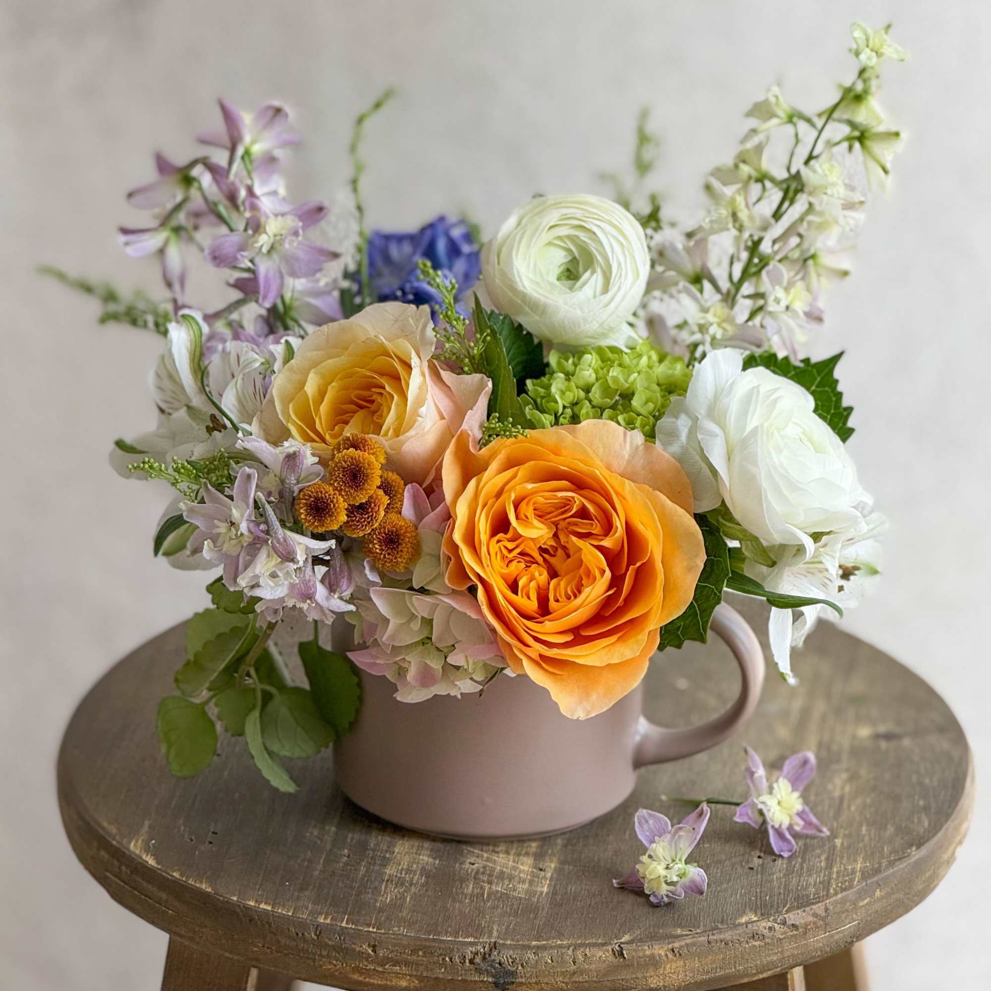 Mixed bouquet of orange, white, and lavender flowers in a pink mug