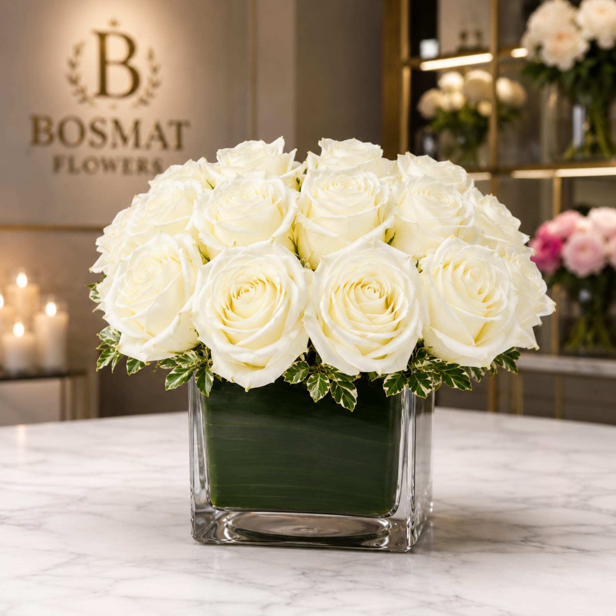 White roses arranged in a square glass vase with variegated foliage