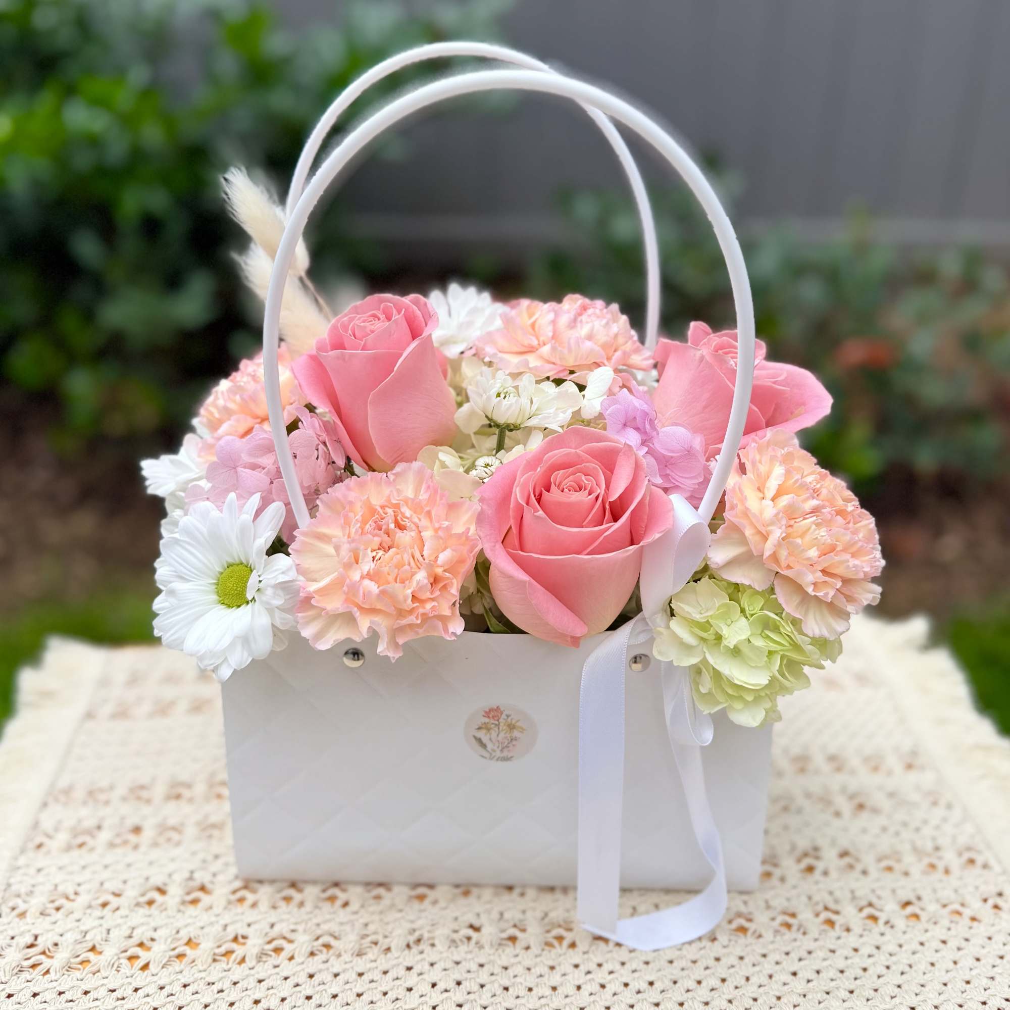 Pink roses and pastel flowers arranged in a white basket with ribbon