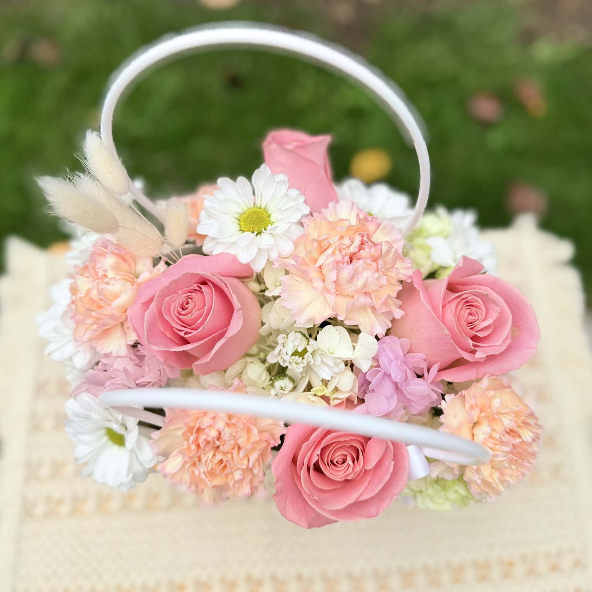 Pink roses and pastel flowers arranged in a white handled basket