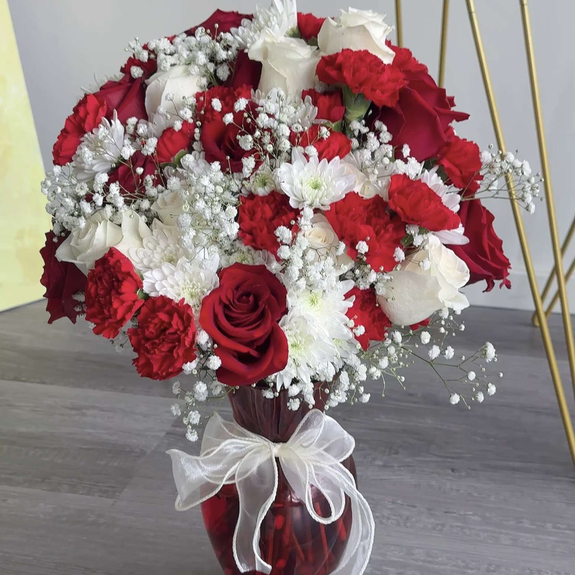 Red and white rose bouquet in a red glass vase with a white ribbon