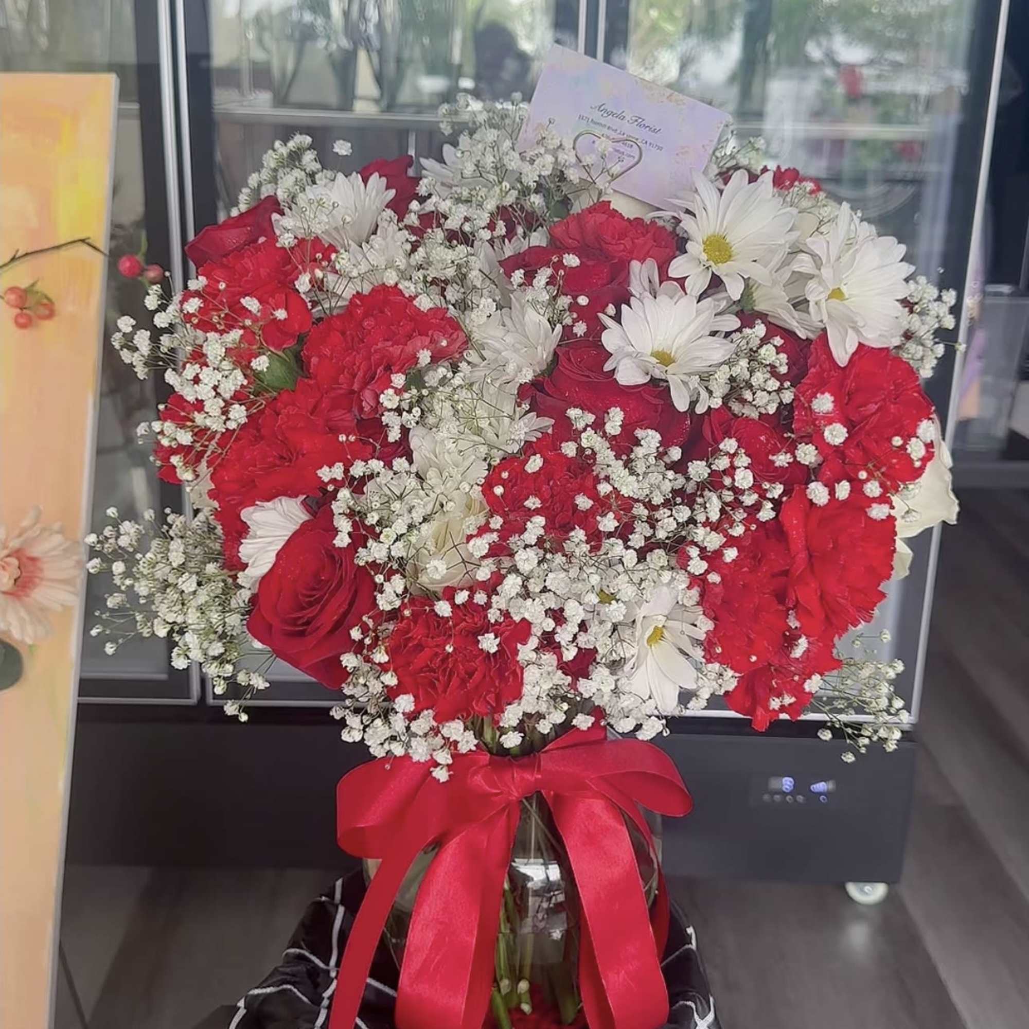 Red and white bouquet in a glass vase with a red ribbon