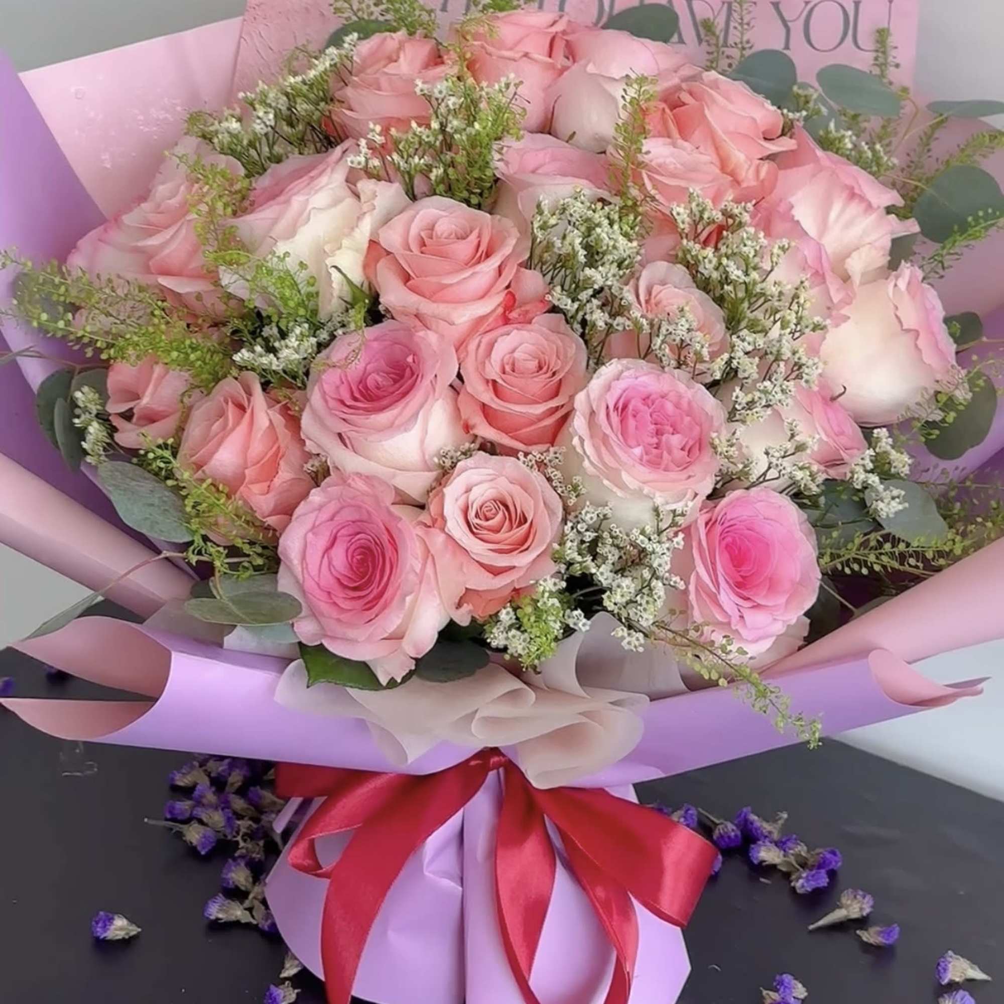 Pink rose bouquet wrapped in lavender paper with a red ribbon