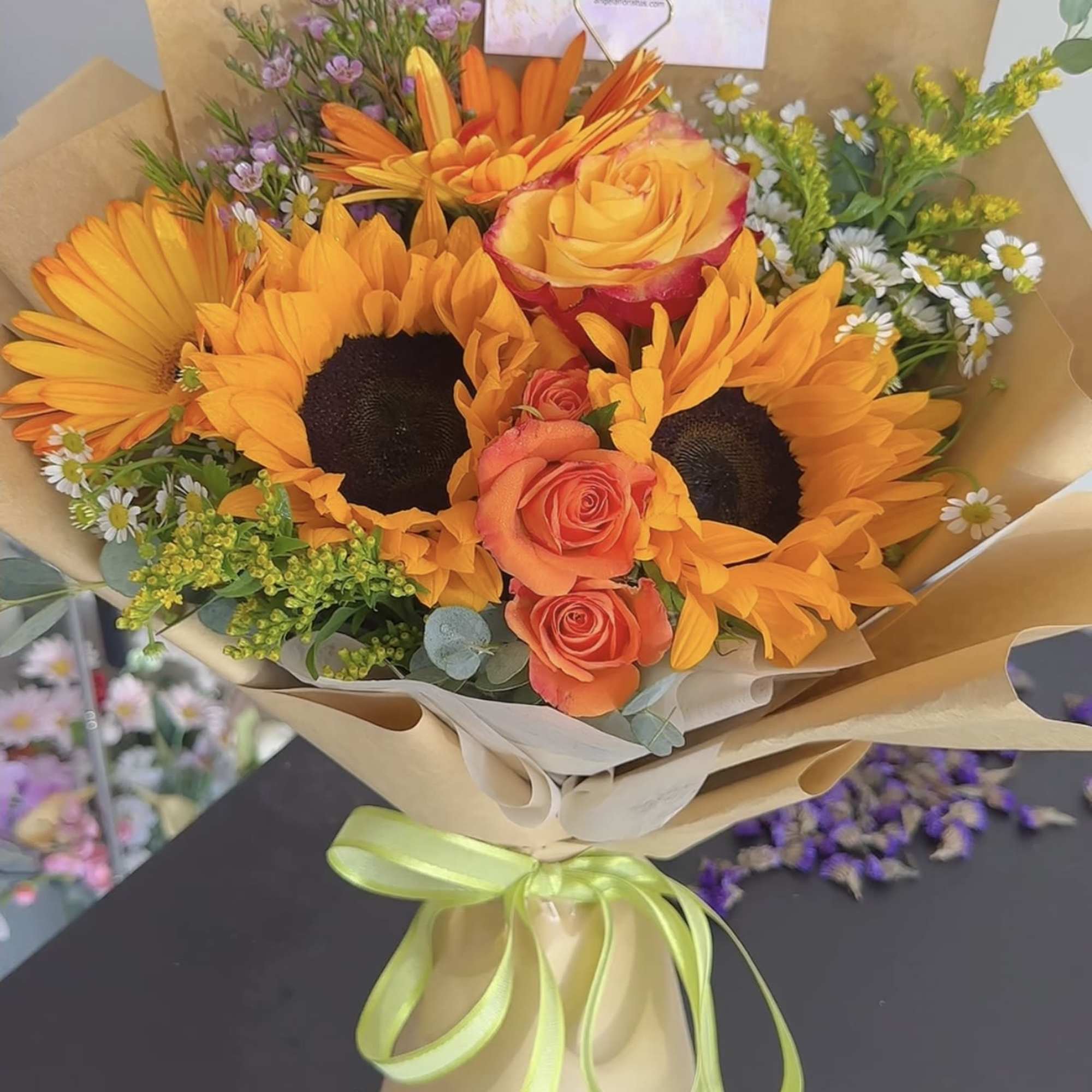 Bouquet of orange sunflowers and roses wrapped in tan paper