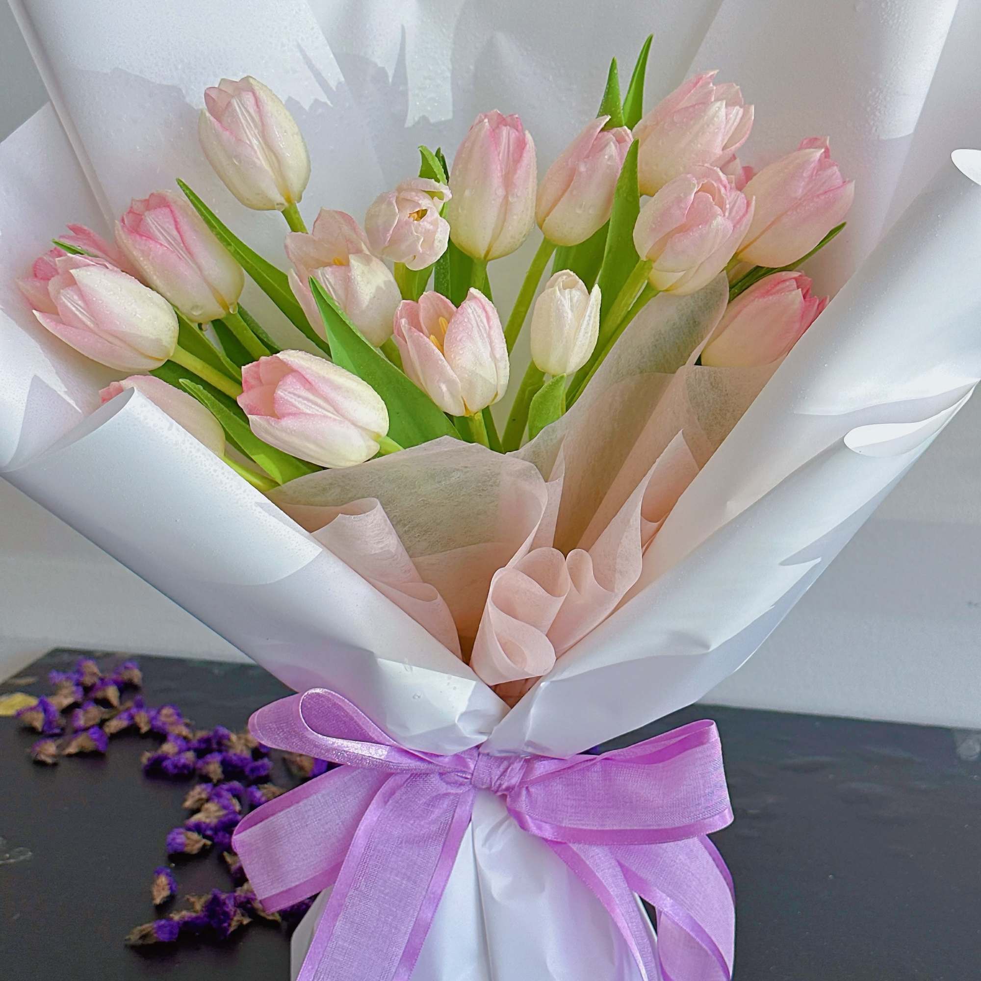 Bouquet of pale pink tulips wrapped in white paper with a lavender ribbon