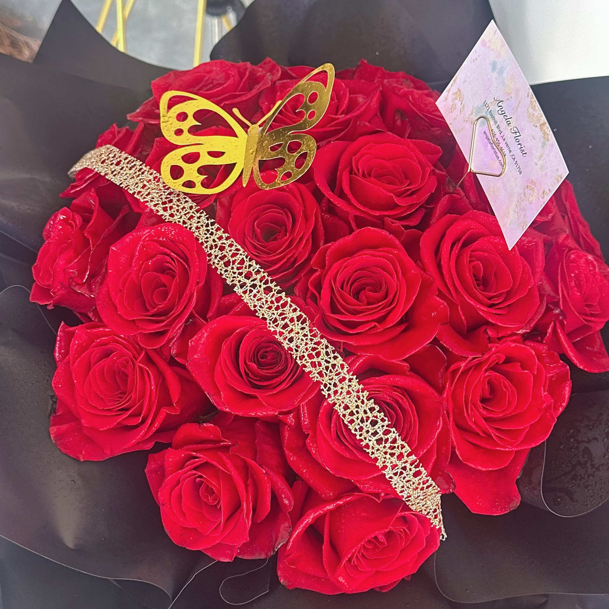 Bouquet of red roses wrapped in black paper with a gold butterfly decoration