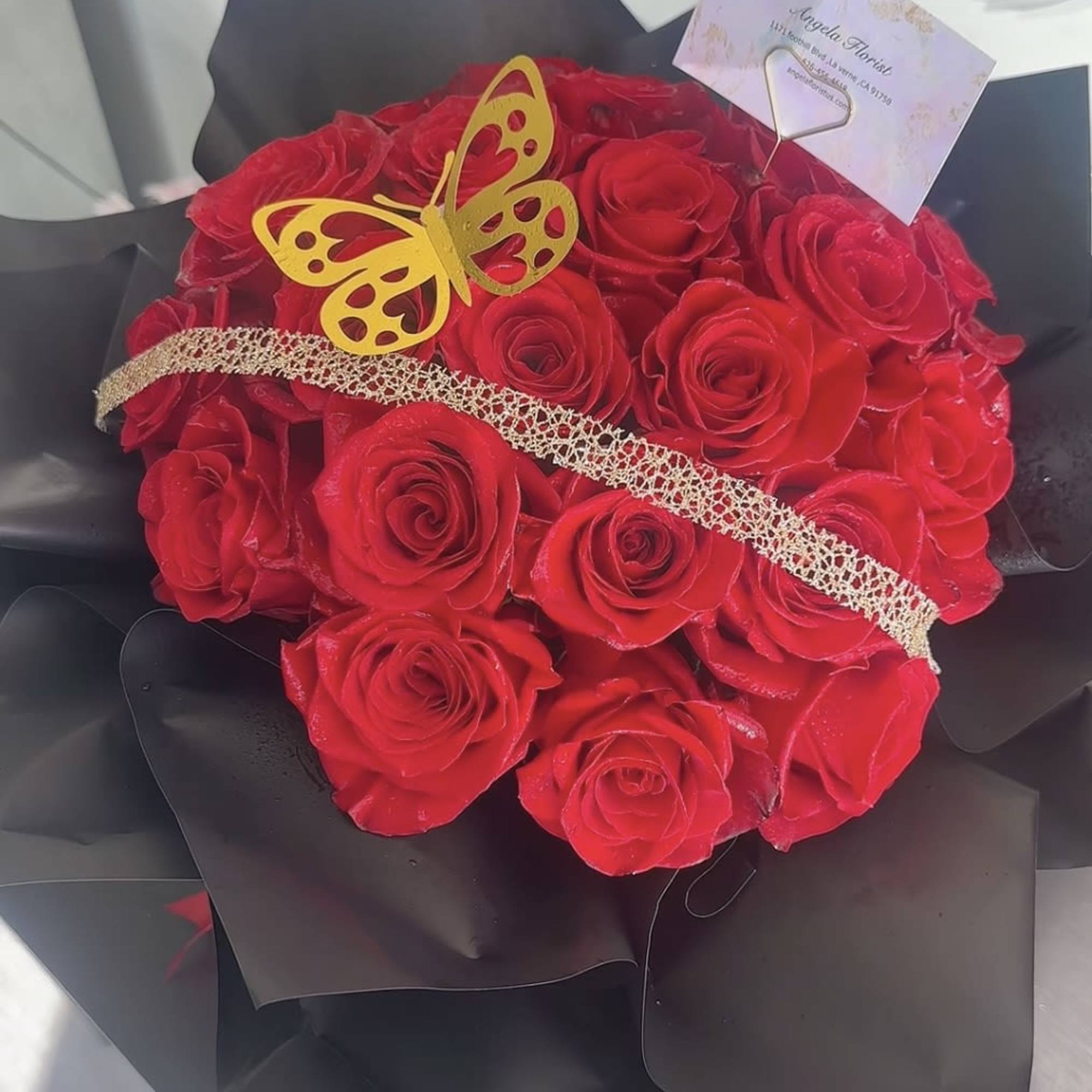 Bouquet of red roses wrapped in black paper with a gold butterfly accent