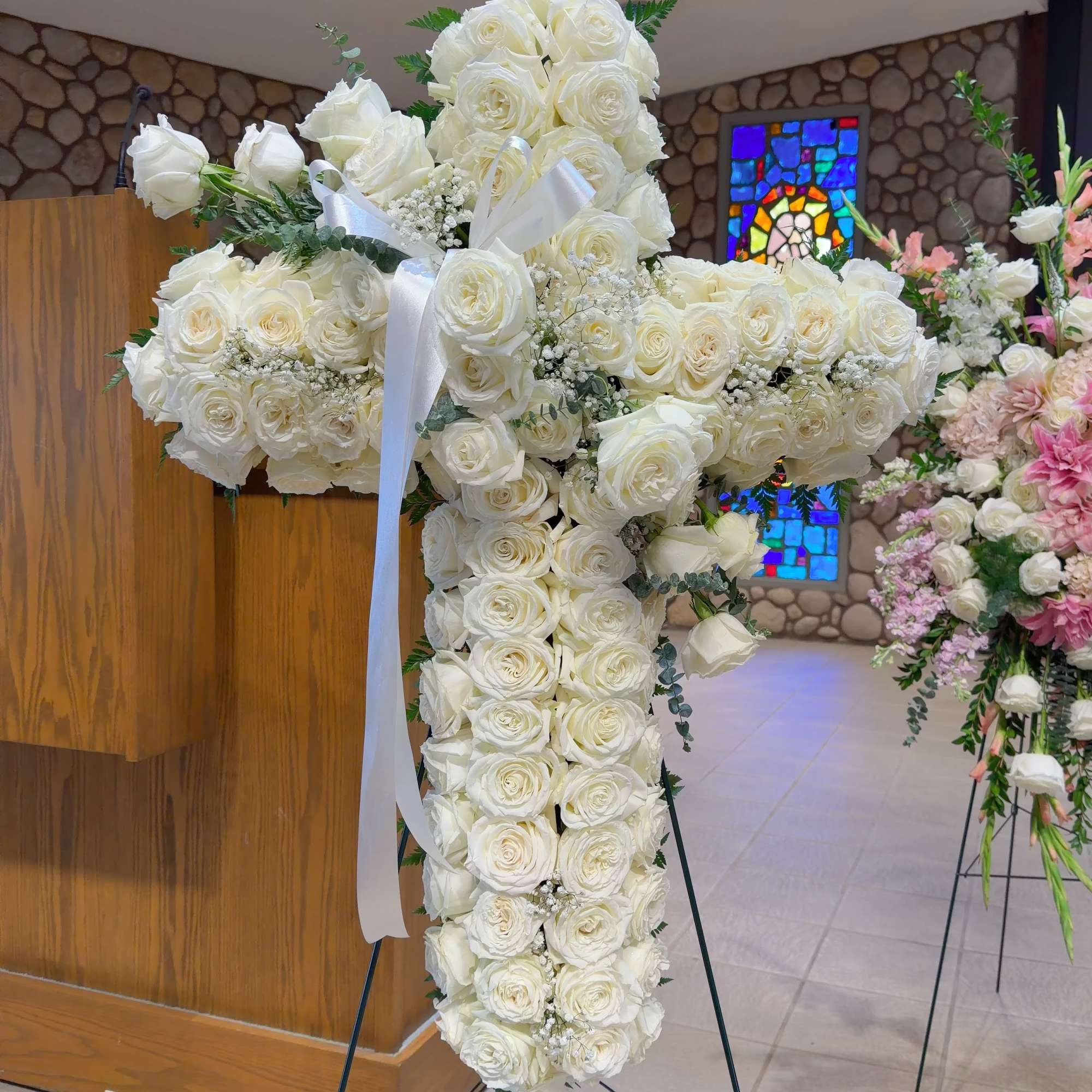 White rose cross on a stand with a white ribbon