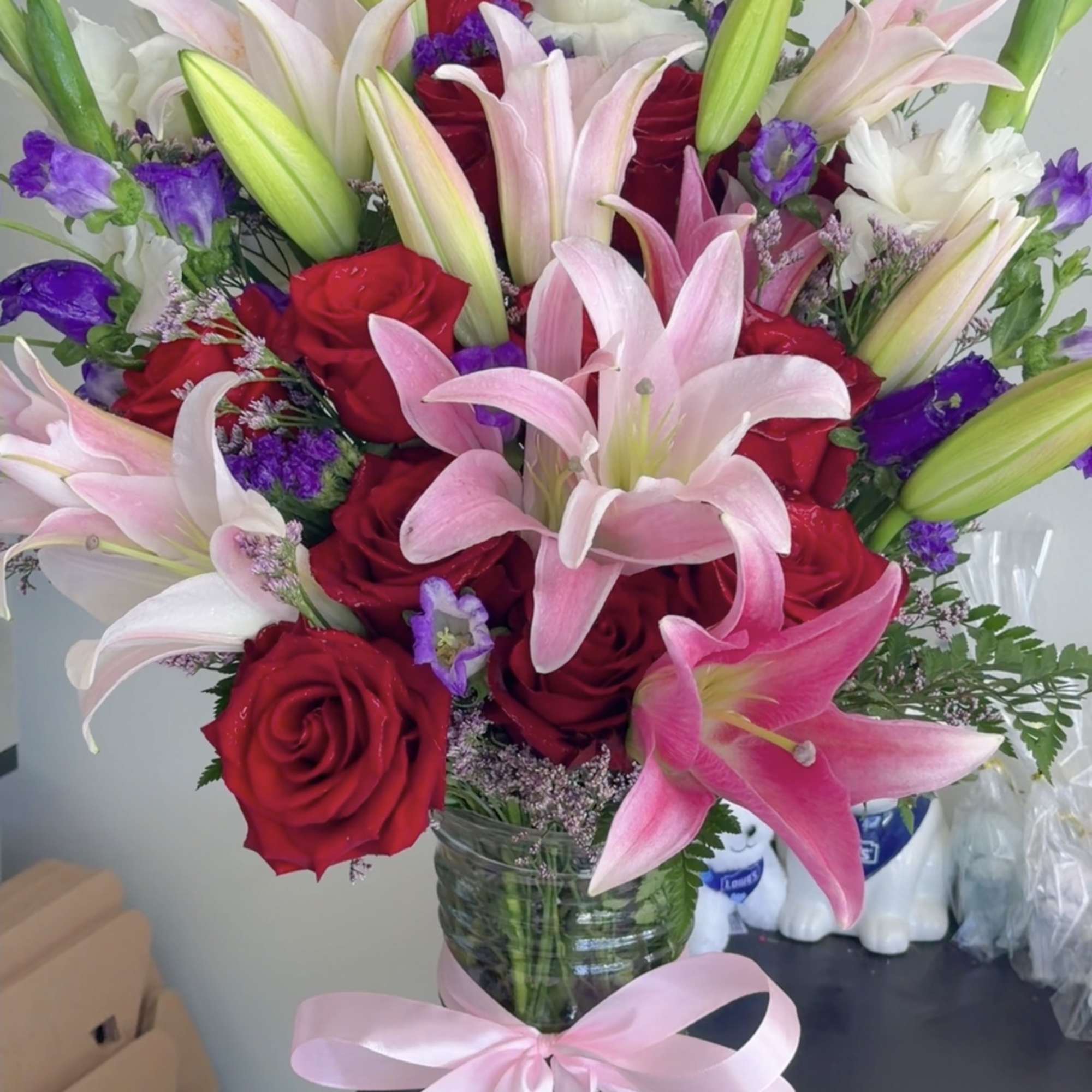 Bouquet of red roses and pink lilies in a glass vase with a pink ribbon